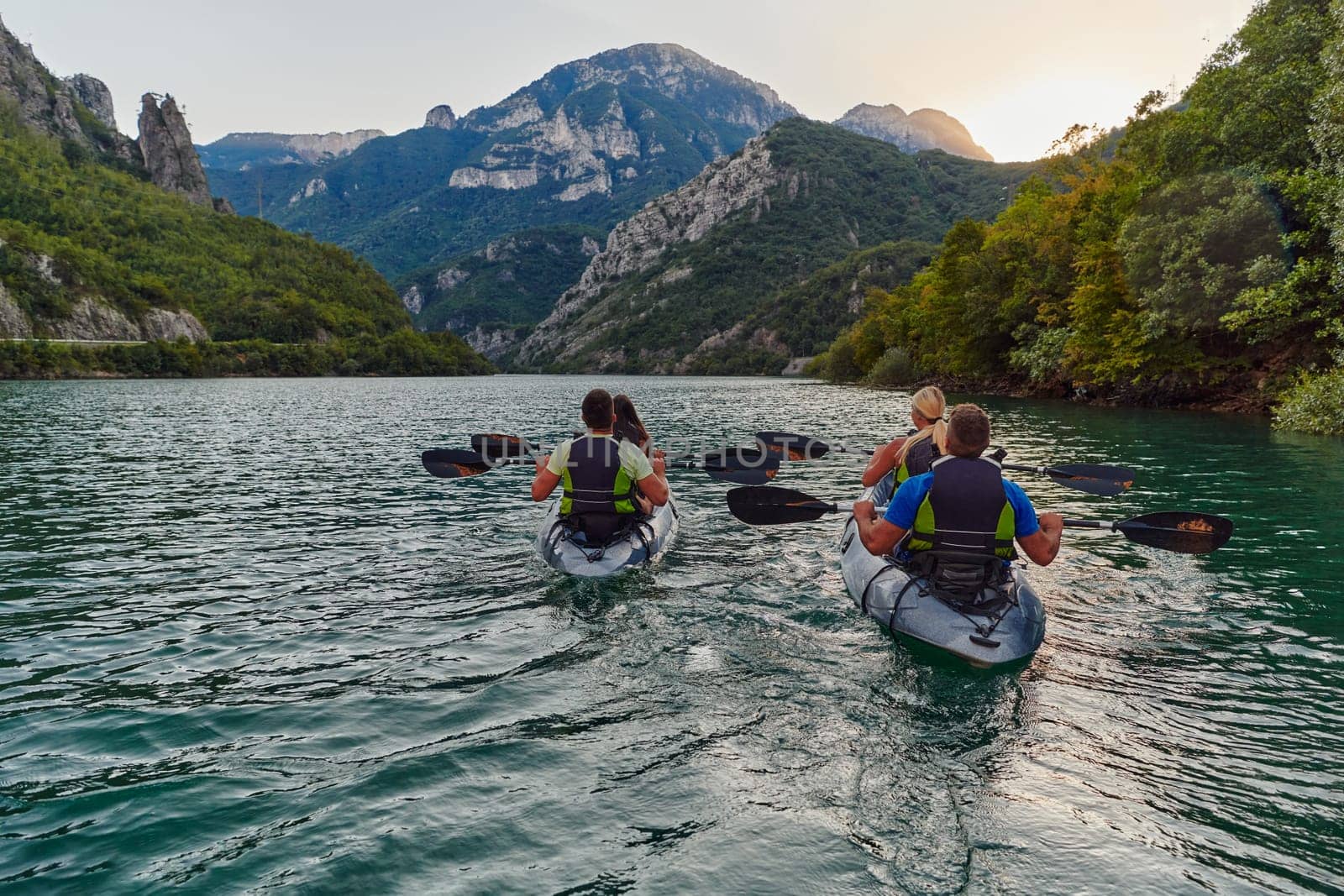 A group of friends enjoying fun and kayaking exploring the calm river, surrounding forest and large natural river canyons during an idyllic sunset