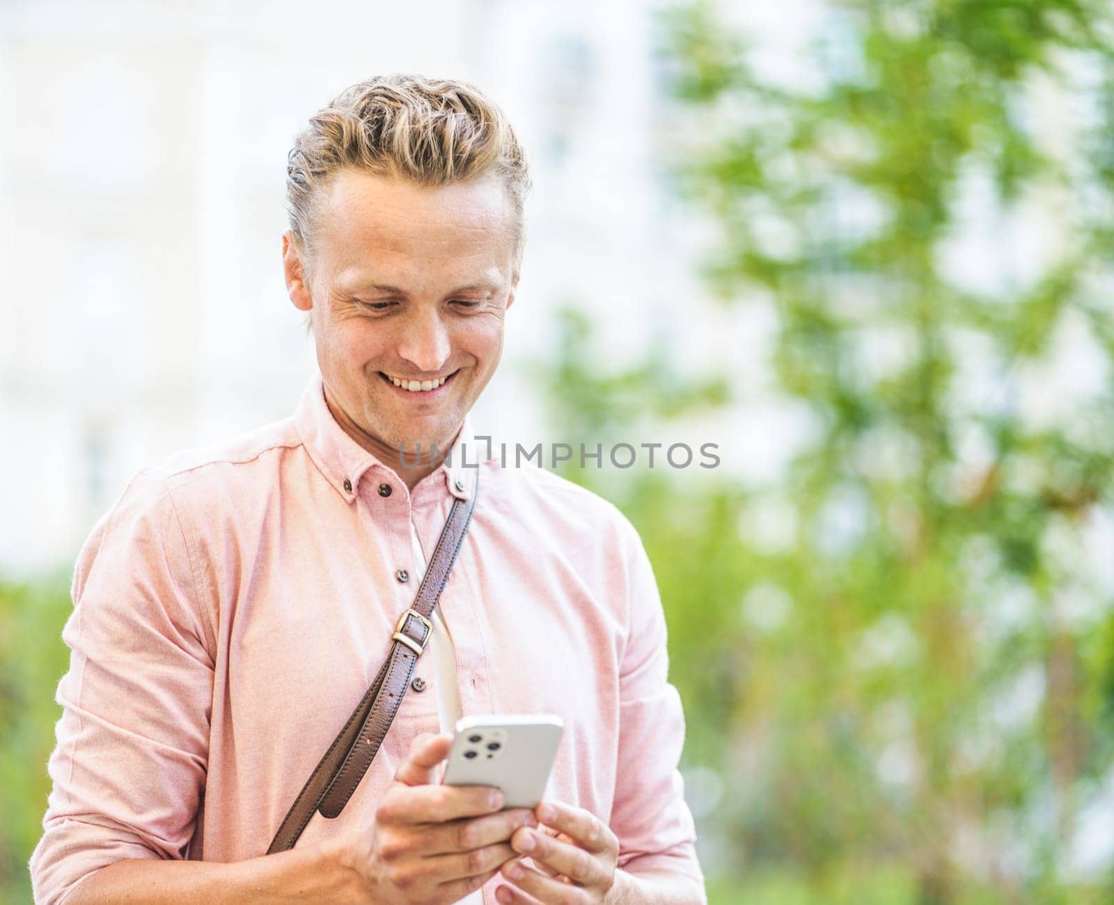 Happy man texting message on phone while standing across street in urban city. Concept of easy communication in urban setting. Man's expression reflects happiness while engaging in effortless messaging. High quality photo