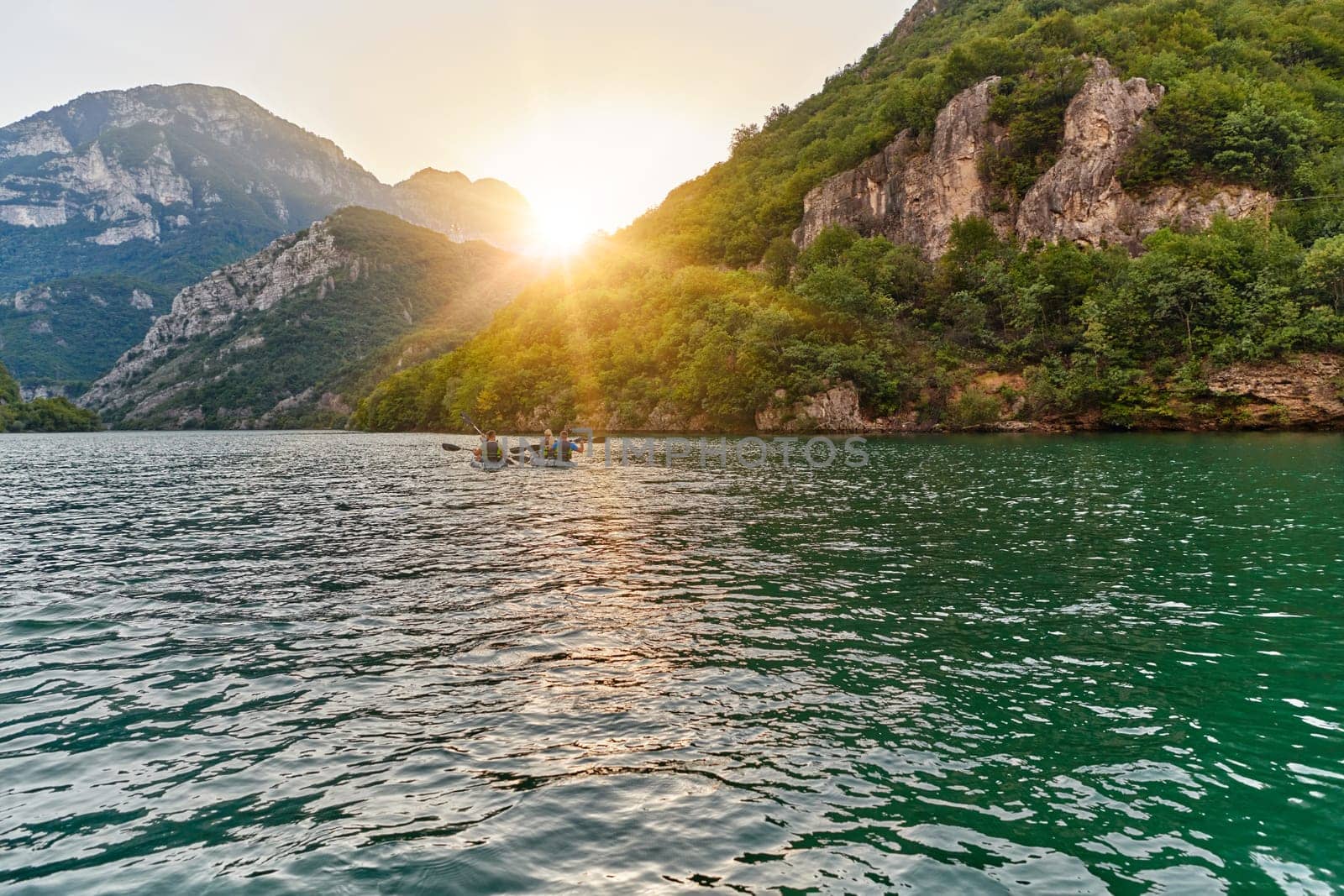 A group of friends enjoying fun and kayaking exploring the calm river, surrounding forest and large natural river canyons during an idyllic sunset