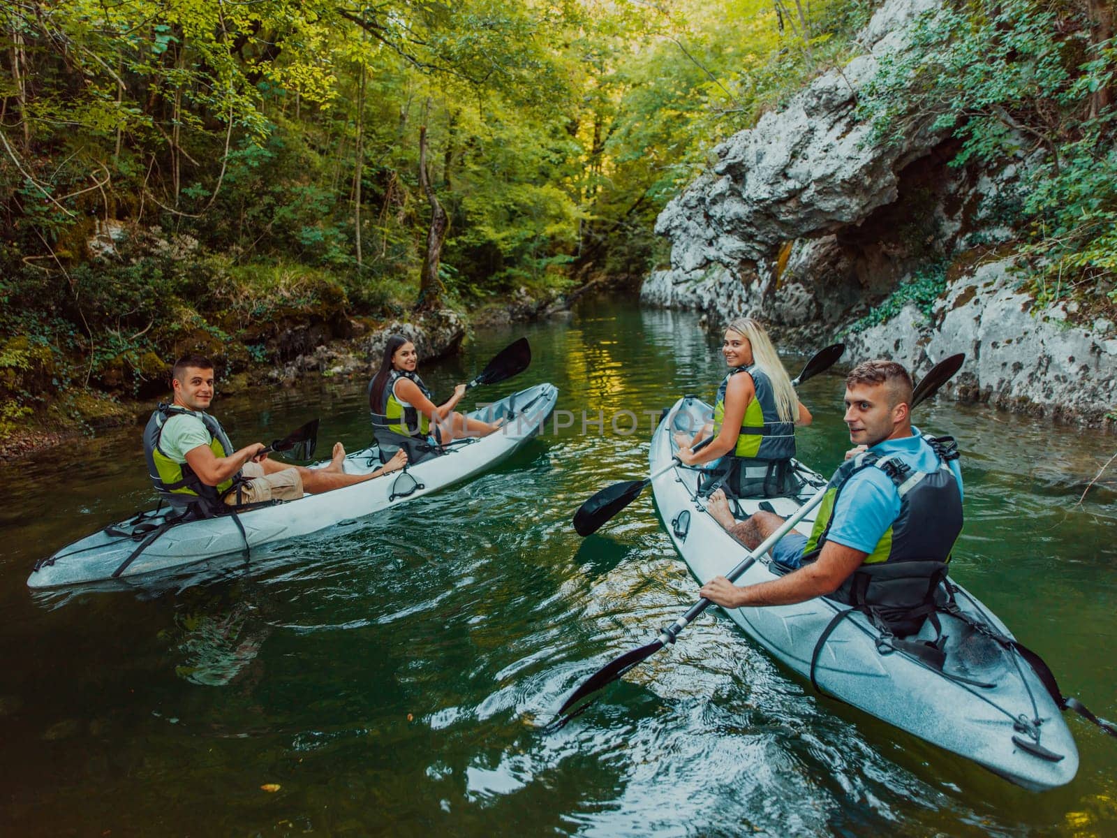 A group of friends enjoying having fun and kayaking while exploring the calm river, surrounding forest and large natural river canyons.