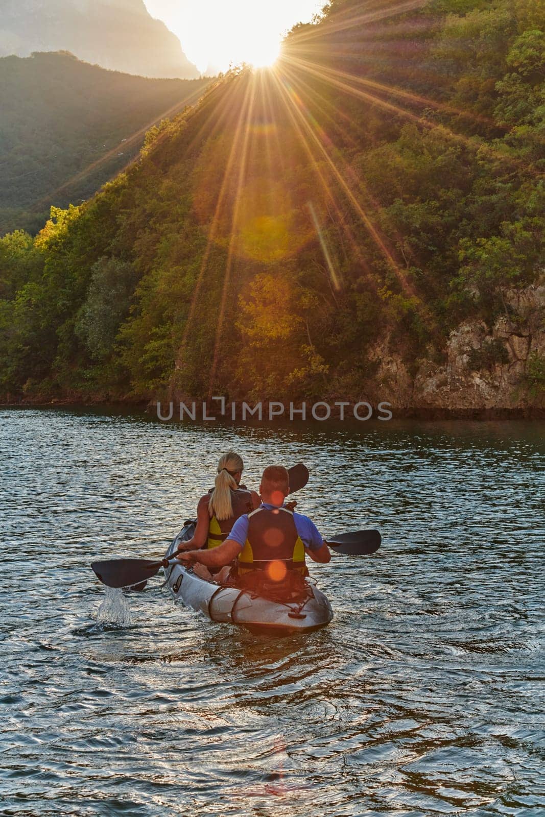 A young couple enjoying an idyllic kayak ride in the middle of a beautiful river surrounded by forest greenery in sunset time.