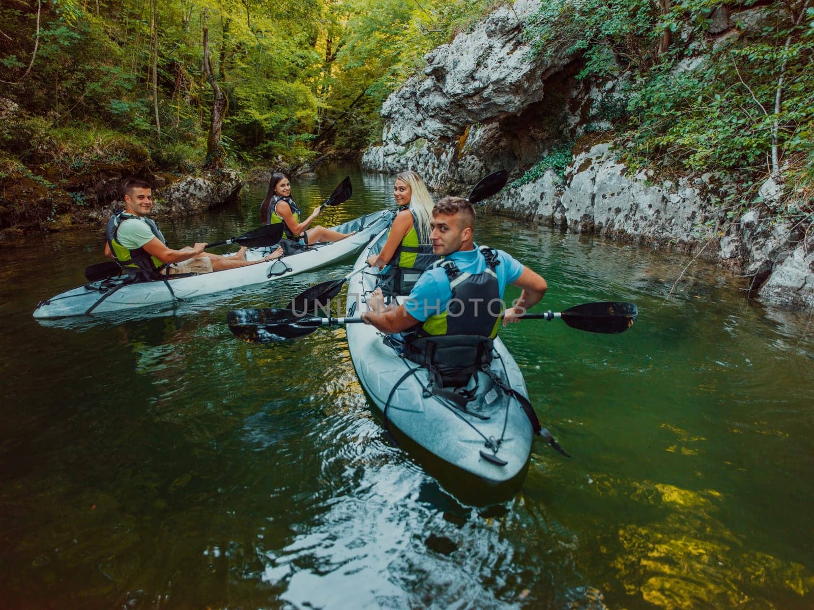 A group of friends enjoying having fun and kayaking while exploring the calm river, surrounding forest and large natural river canyons.