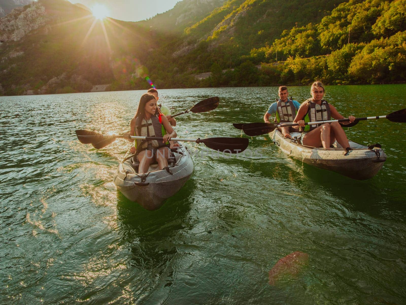 A group of friends enjoying fun and kayaking exploring the calm river, surrounding forest and large natural river canyons during an idyllic sunset