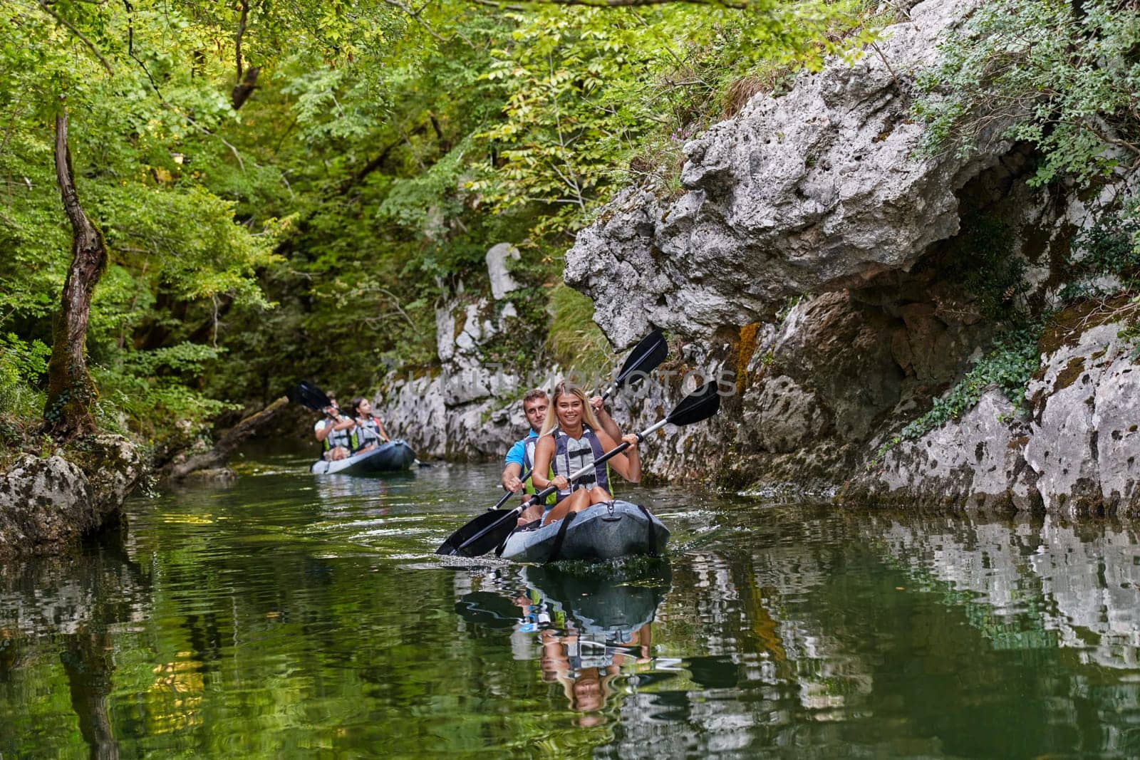 A group of friends enjoying having fun and kayaking while exploring the calm river, surrounding forest and large natural river canyons.