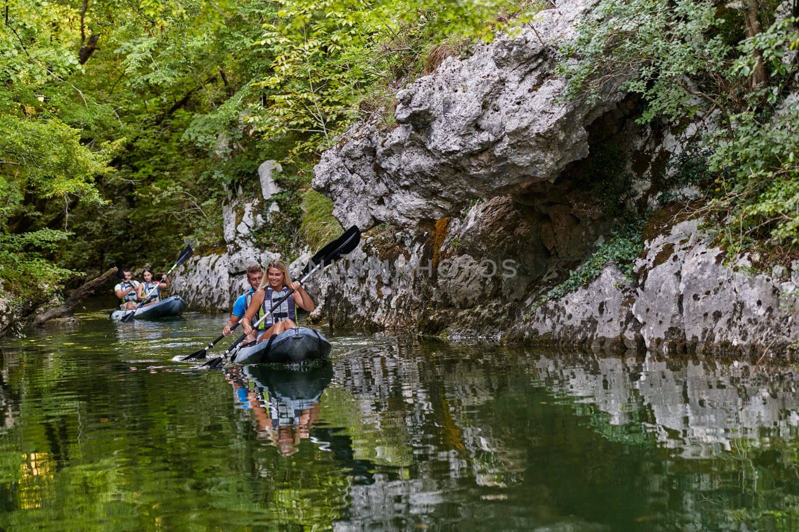 A group of friends enjoying having fun and kayaking while exploring the calm river, surrounding forest and large natural river canyons by dotshock