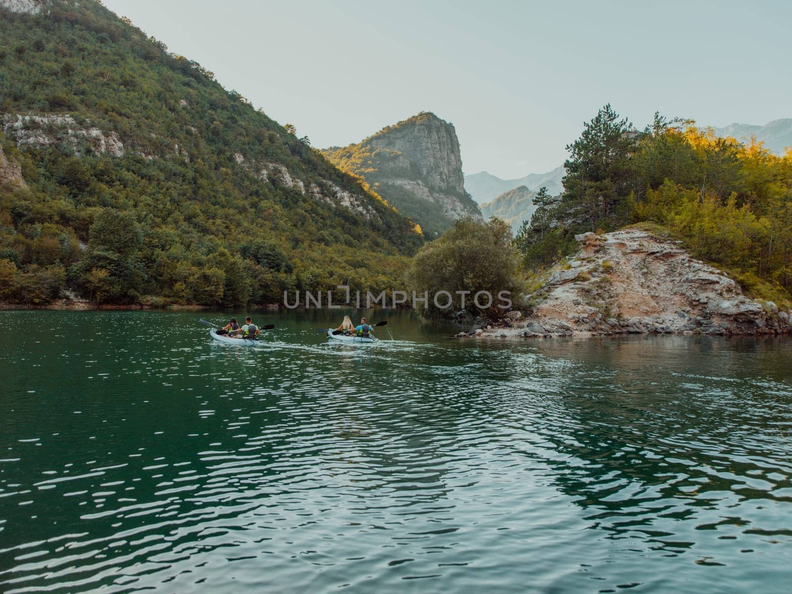 A group of friends enjoying having fun and kayaking while exploring the calm river, surrounding forest and large natural river canyons by dotshock