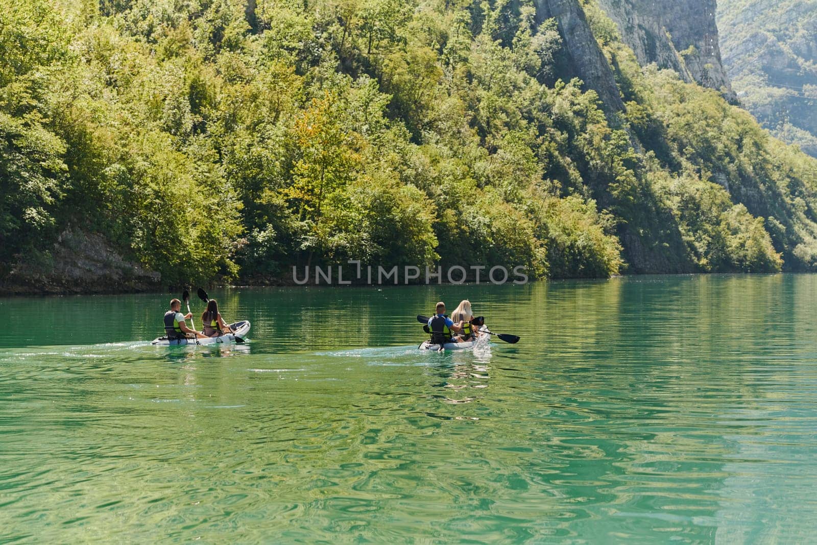 A group of friends enjoying having fun and kayaking while exploring the calm river, surrounding forest and large natural river canyons.