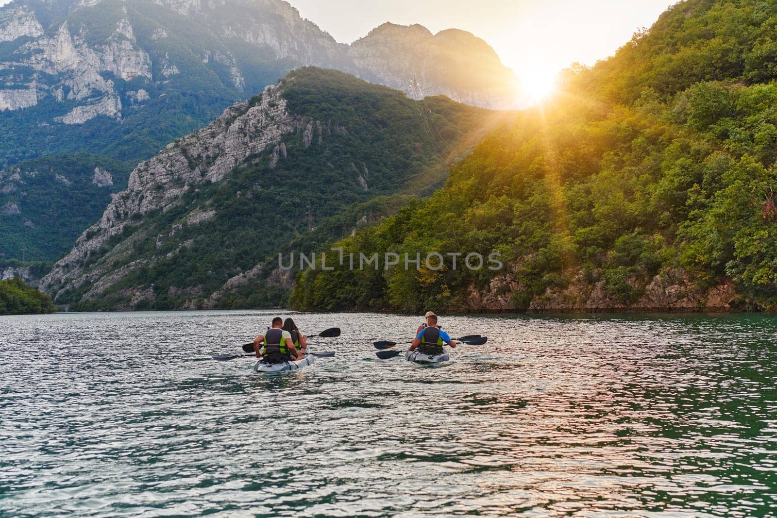 A group of friends enjoying fun and kayaking exploring the calm river, surrounding forest and large natural river canyons during an idyllic sunset