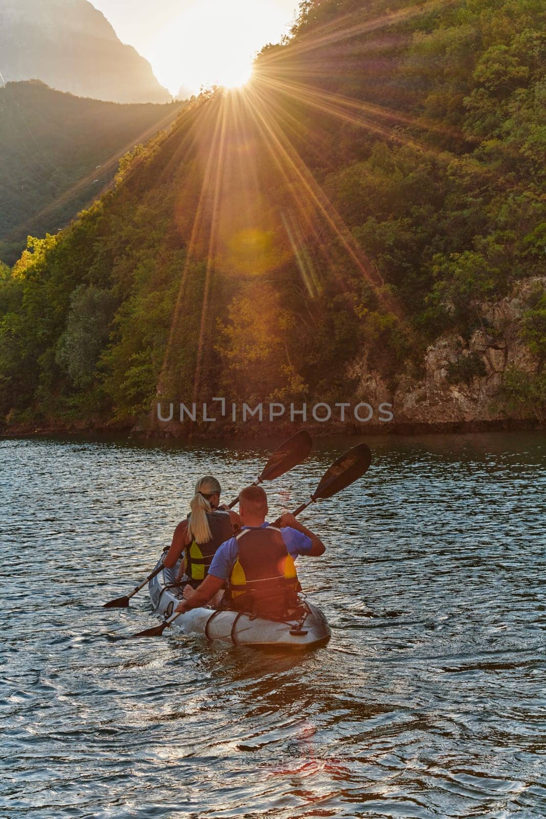 A young couple enjoying an idyllic kayak ride in the middle of a beautiful river surrounded by forest greenery in sunset time by dotshock