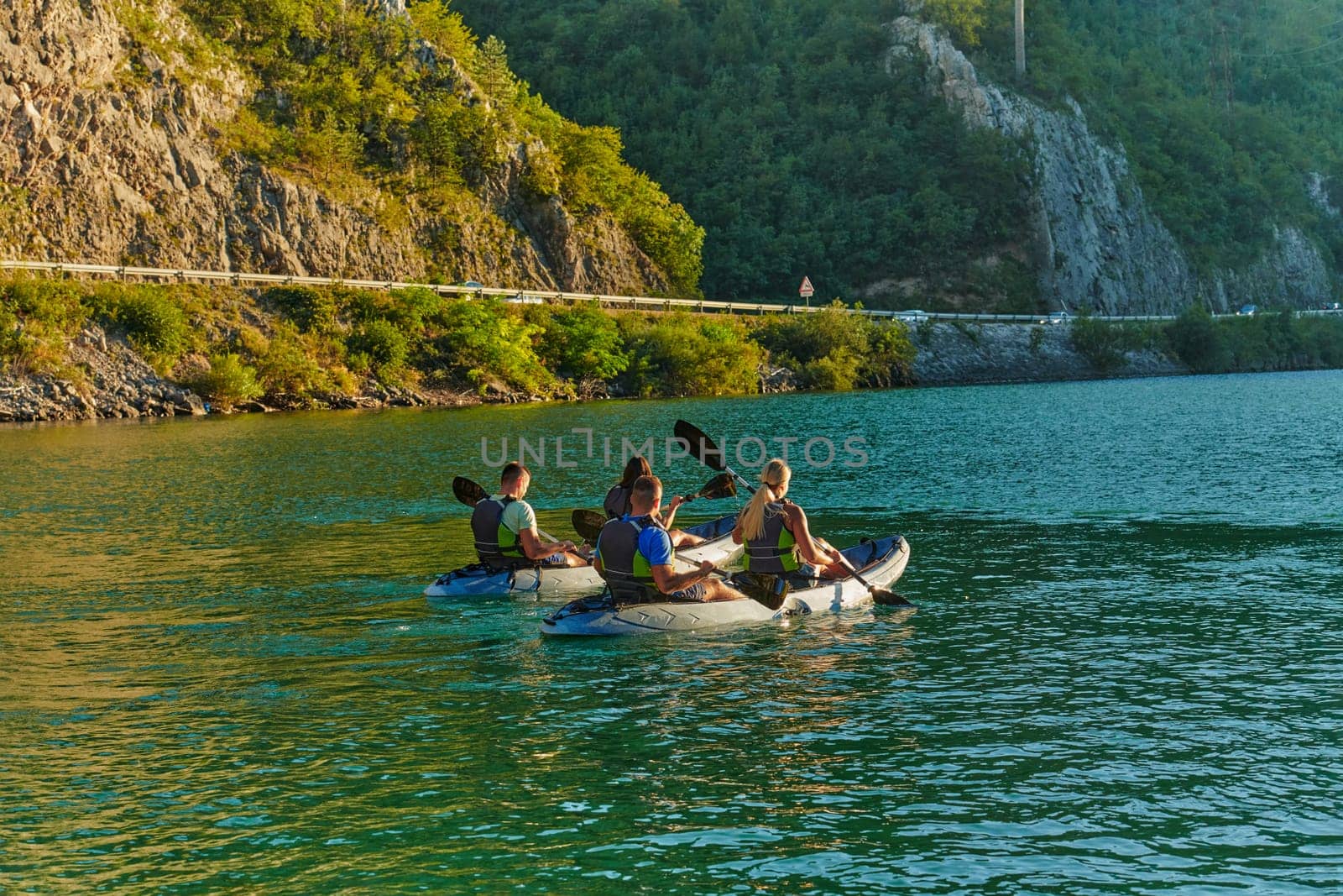 A group of friends enjoying fun and kayaking exploring the calm river, surrounding forest and large natural river canyons during an idyllic sunset