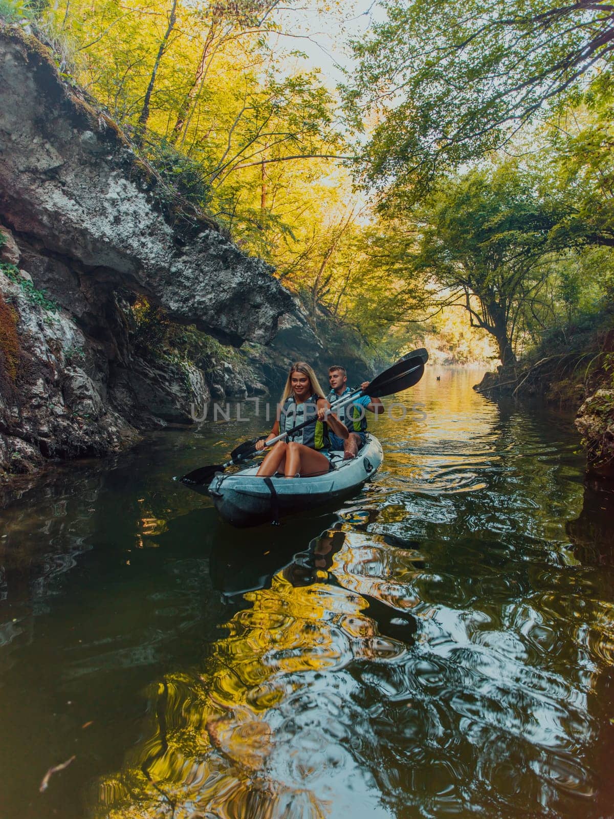 A young couple enjoying an idyllic kayak ride in the middle of a beautiful river surrounded by forest greenery.