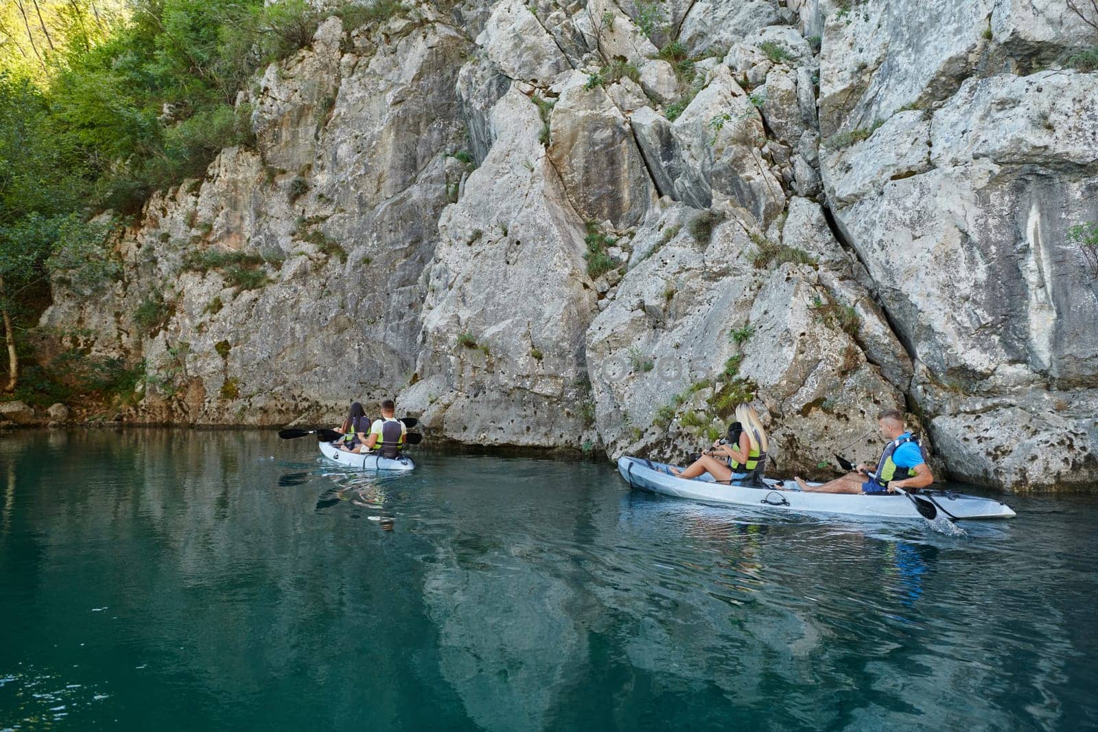 A group of friends enjoying having fun and kayaking while exploring the calm river, surrounding forest and large natural river canyons.