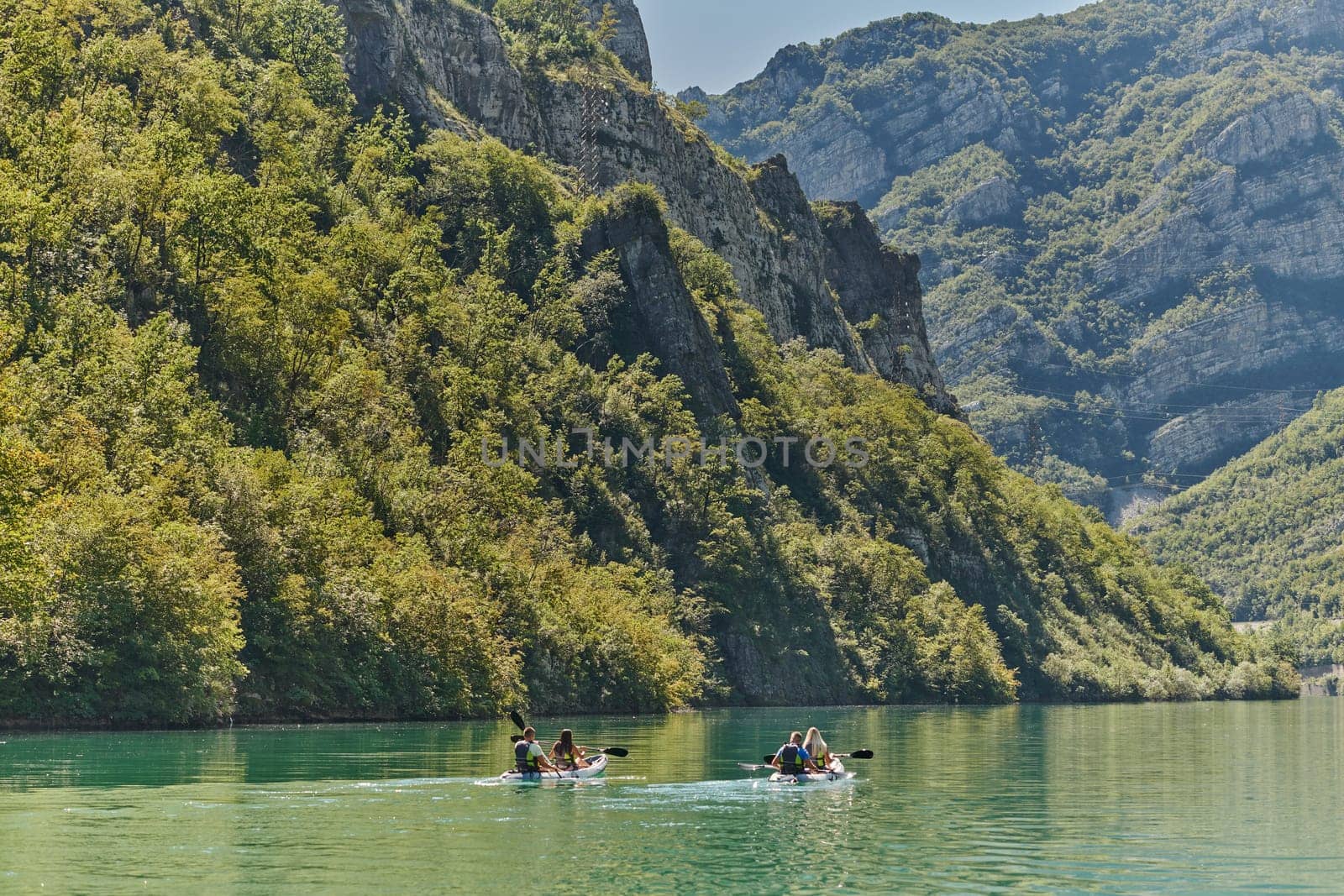 A group of friends enjoying having fun and kayaking while exploring the calm river, surrounding forest and large natural river canyons.