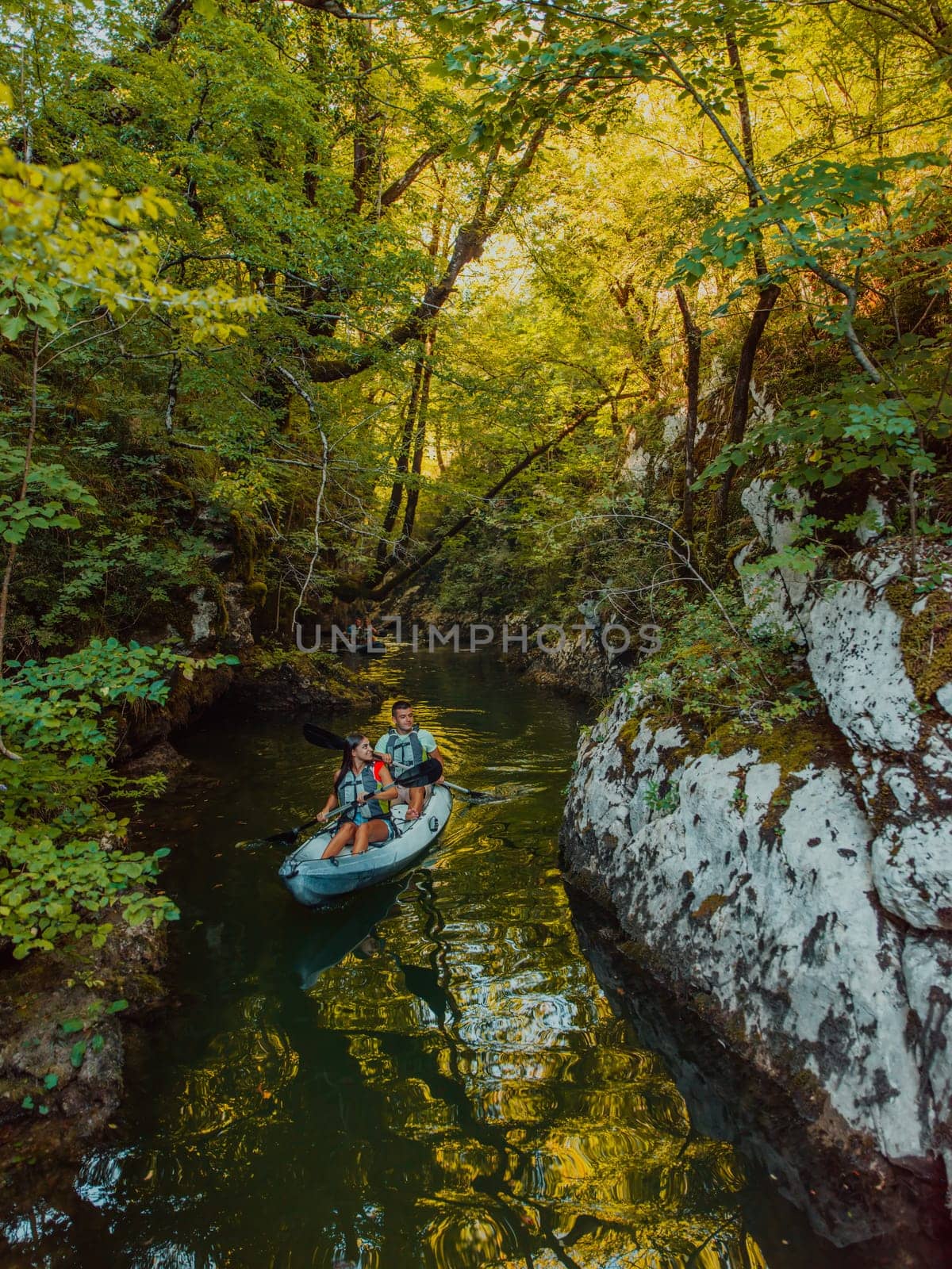 A young couple enjoying an idyllic kayak ride in the middle of a beautiful river surrounded by forest greenery by dotshock