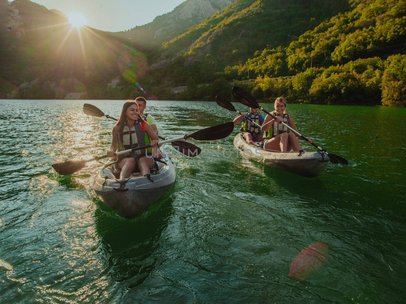 A group of friends enjoying fun and kayaking exploring the calm river, surrounding forest and large natural river canyons during an idyllic sunset