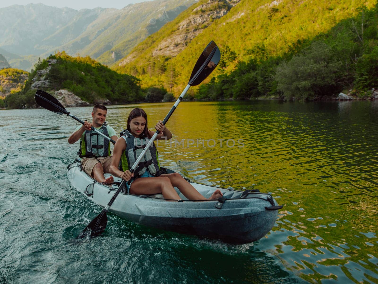 A young couple enjoying an idyllic kayak ride in the middle of a beautiful river surrounded by forest greenery.