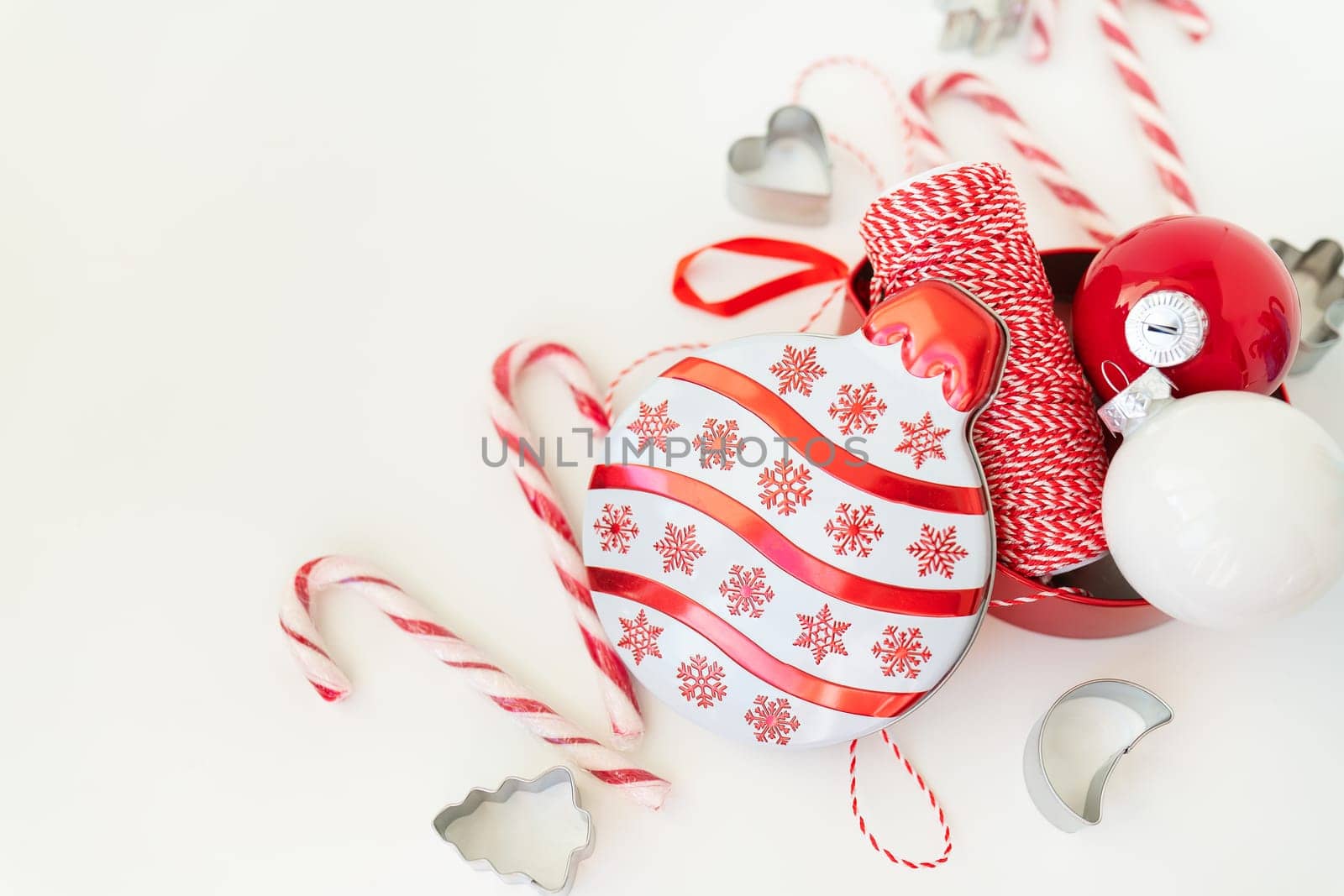 Christmas candies, along with cookie cutters, Christmas tree toys and red thread for gift wrapping, lie on a white table. Selective focus, noise. Christmas and New Year 2023-2024. Place for an inscription
