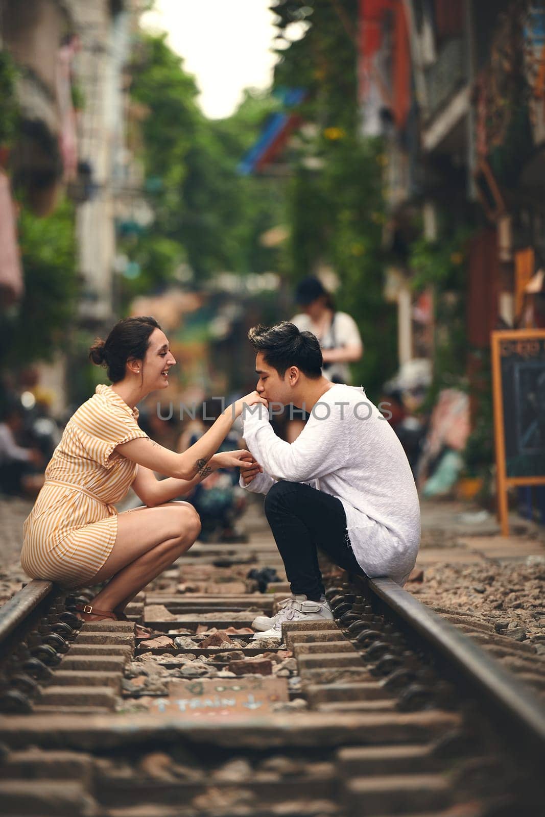 Theyre at romance station now. a young couple sharing a romantic moment on the train tracks in the streets of Vietnam. by YuriArcurs