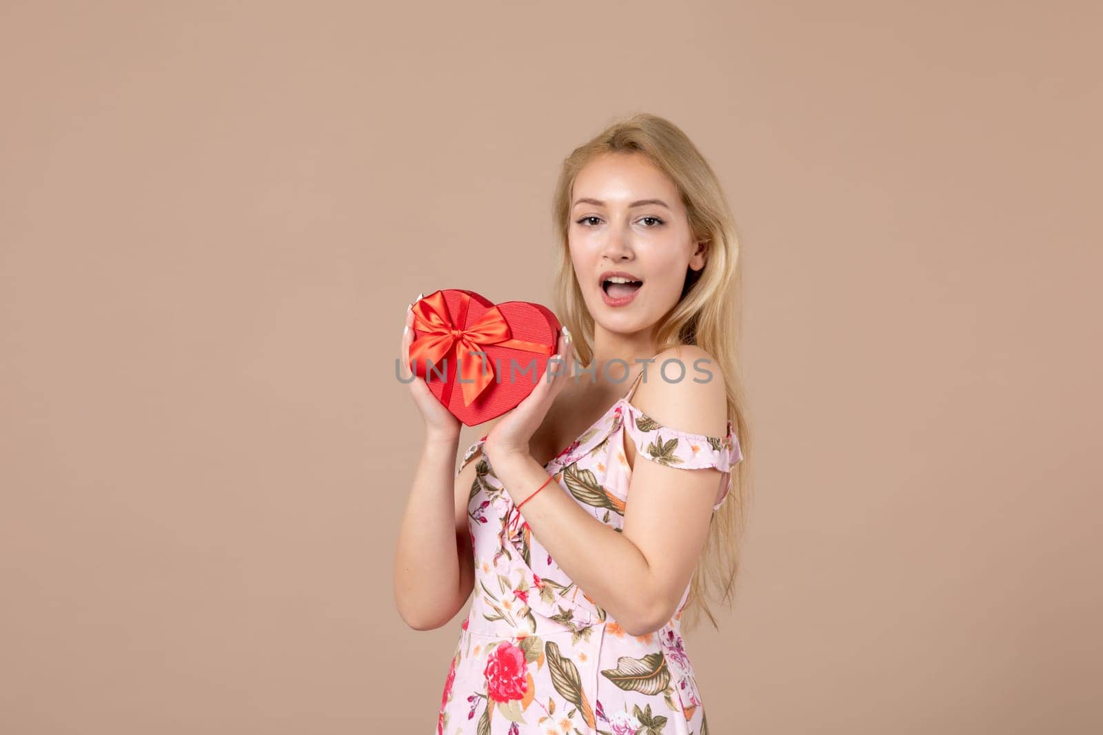 front view young female holding red heart shaped present on brown background feminine sensual money march woman equality horizontal marriage by Kamran