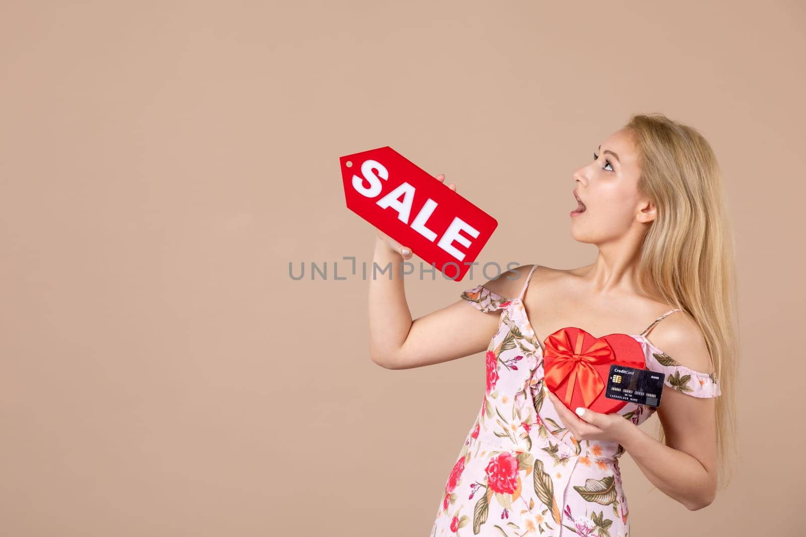 front view young female holding red present sale nameplate and bank card on brown background money march horizontal feminine sensual shopping woman