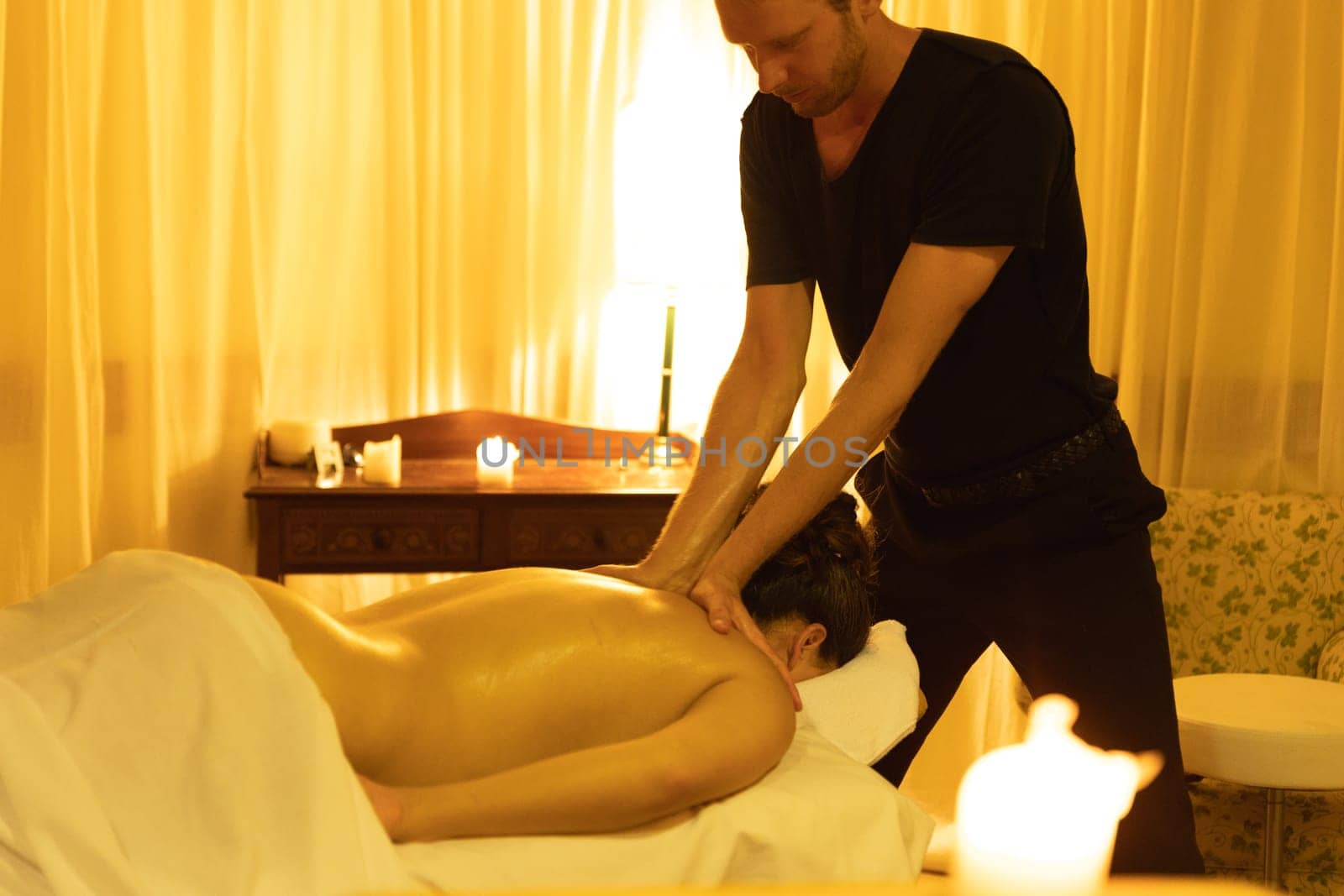 Massage session in SPA salon - a man massaging the upper area of bare back of a woman. Mid shot