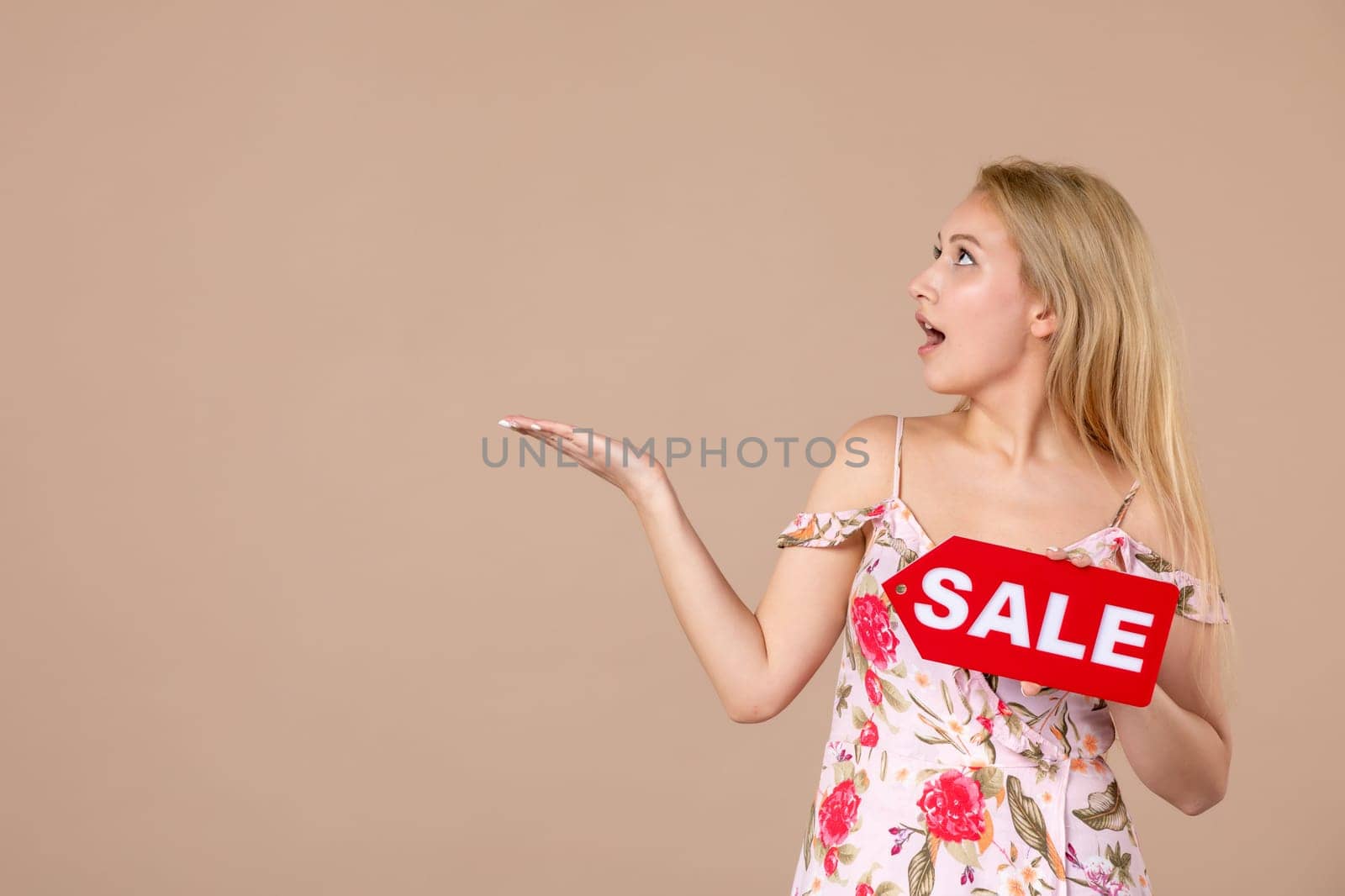 front view young female holding red sale nameplate on brown background march horizontal feminine sensual shopping woman equality by Kamran