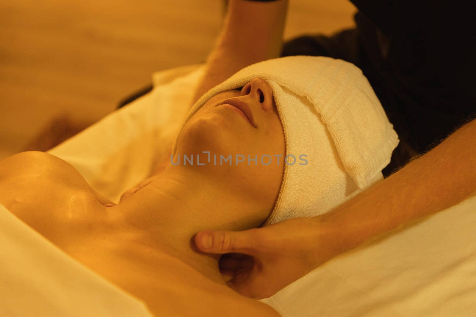 Massage procedure - woman client having a towel on her head while the therapist massaging her neck. Mid shot
