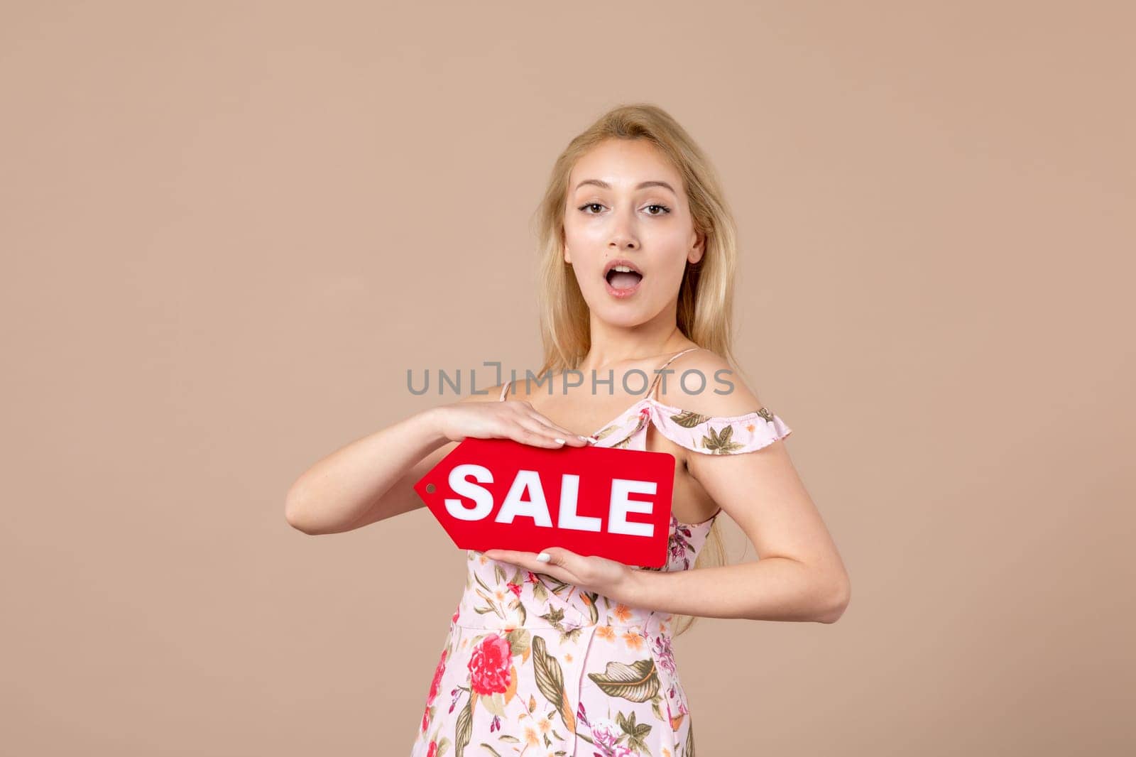 front view young female holding red sale nameplate on brown background money march horizontal feminine equality sensual shopping by Kamran