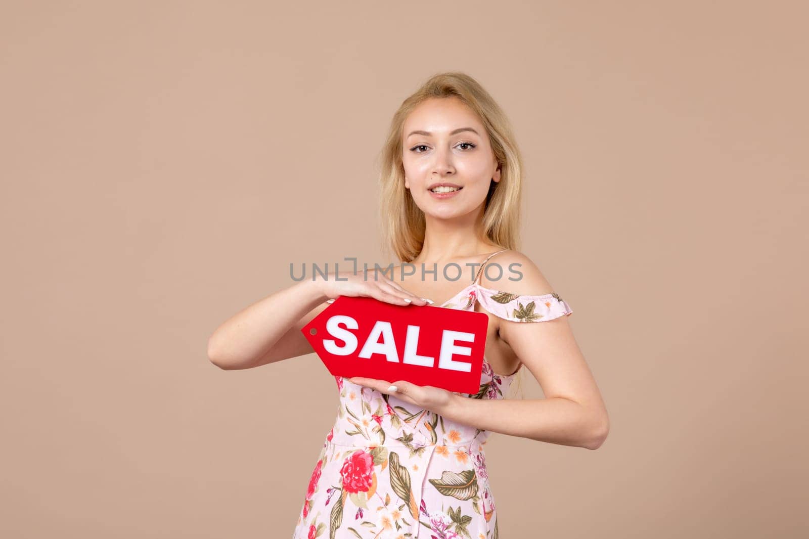 front view young female holding red sale nameplate on brown background money march horizontal feminine equality sensual woman by Kamran