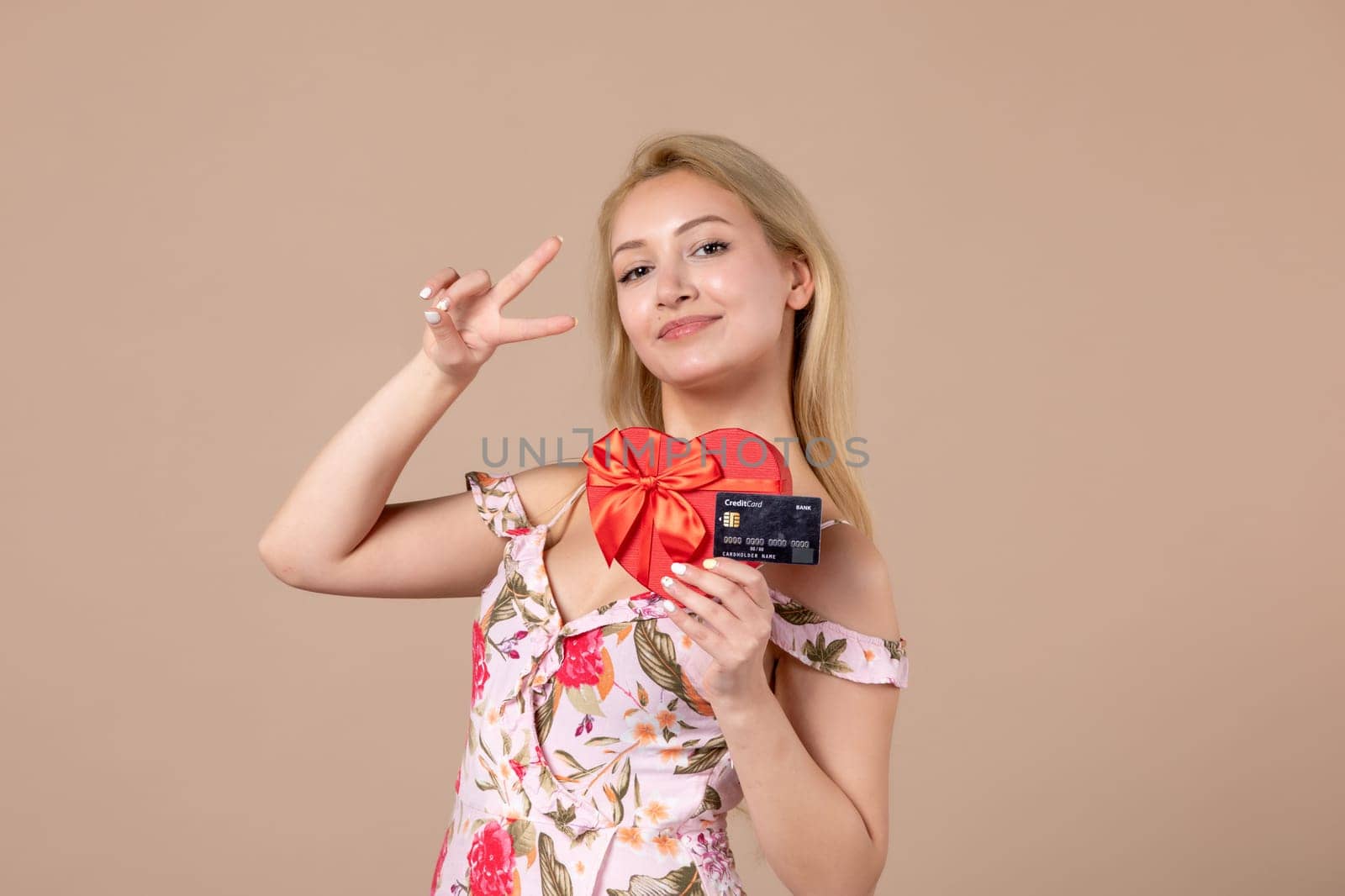 front view young female posing with red heart shaped present and bank card on brown background feminine march woman sensual horizontal equality by Kamran