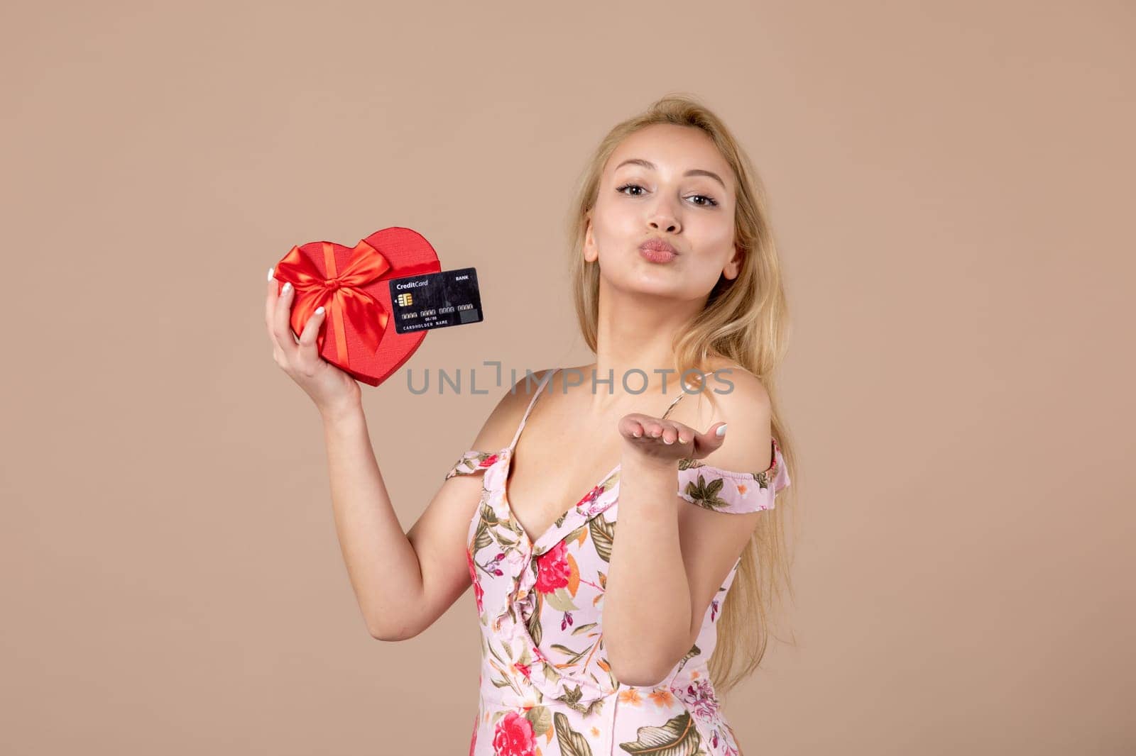 front view young female posing with red heart shaped present and bank card on brown background feminine money march equality sensual horizontal