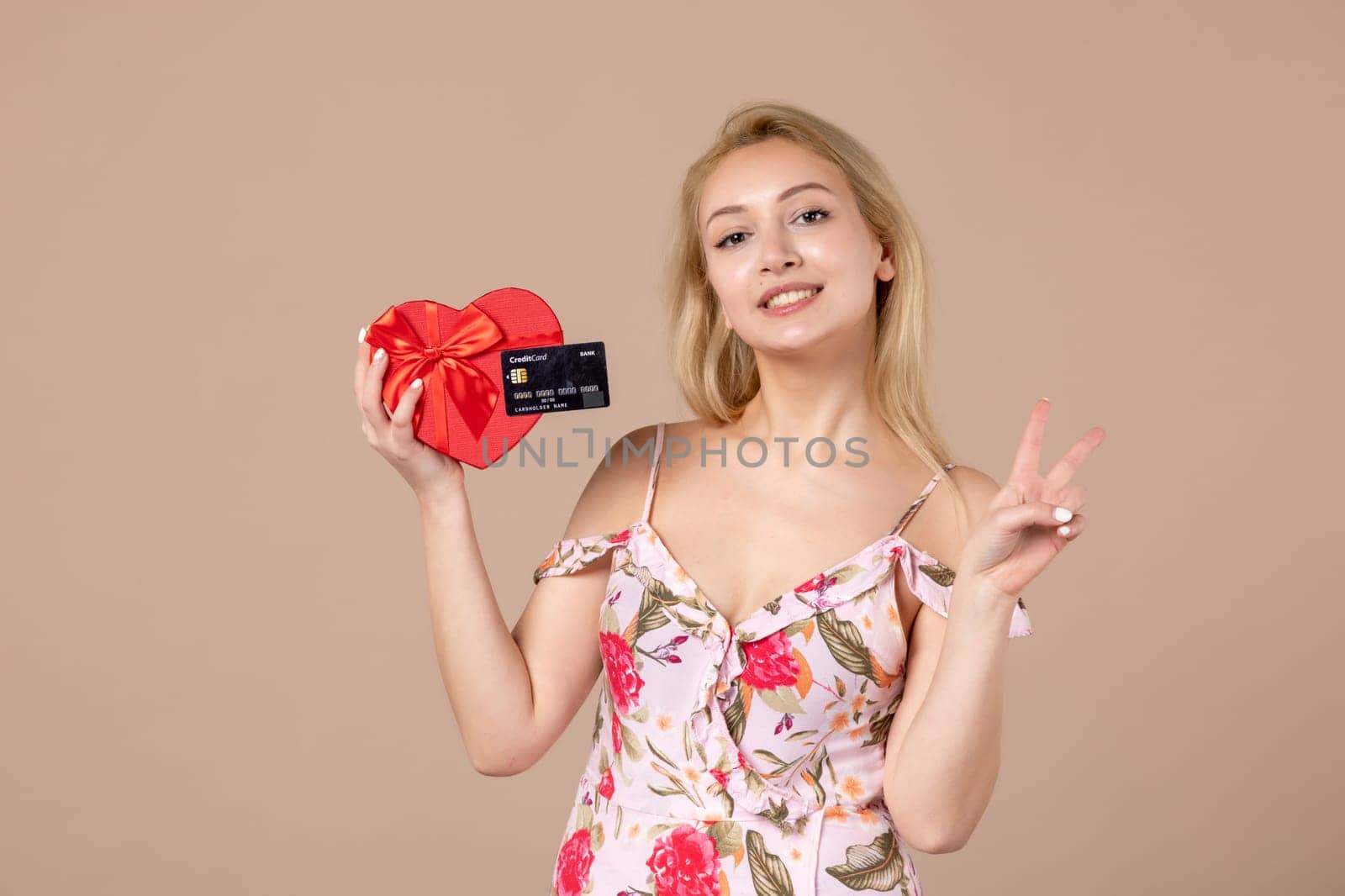 front view young female posing with red heart shaped present and bank card on brown background feminine money march equality woman horizontal