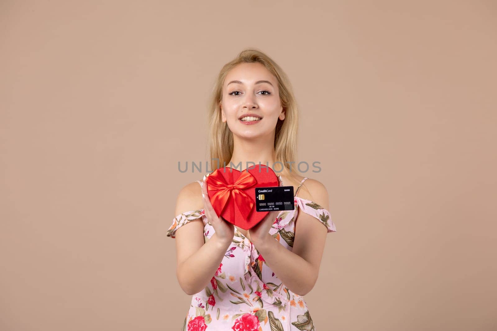front view young female posing with red heart shaped present and bank card on brown background feminine money march equality woman sensual horizontal by Kamran