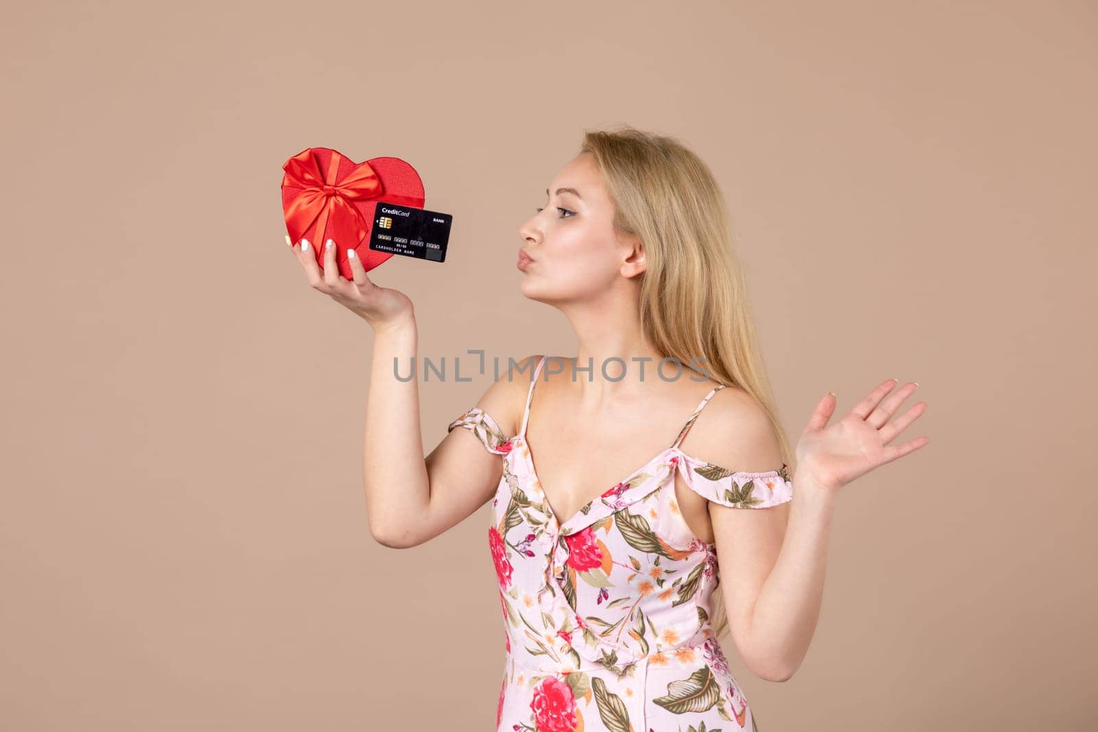 front view young female posing with red heart shaped present and bank card on brown background feminine money march horizontal equality woman