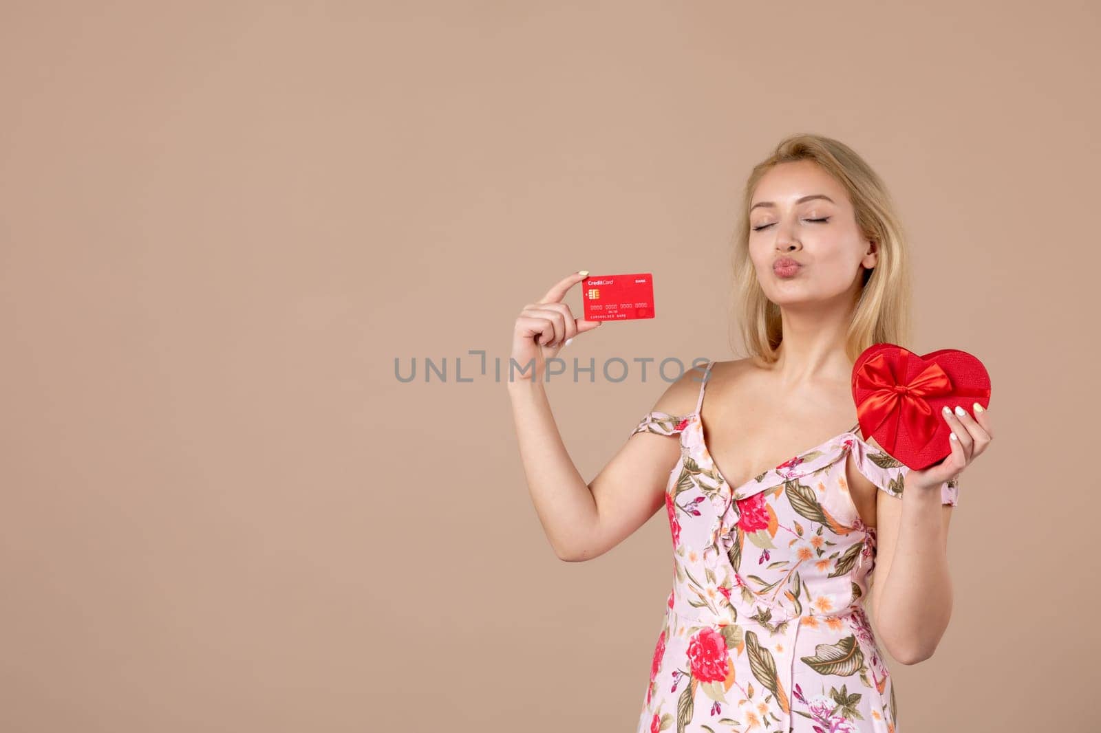 front view young female posing with red heart shaped present and bank card on brown background feminine money march horizontal woman sensual by Kamran