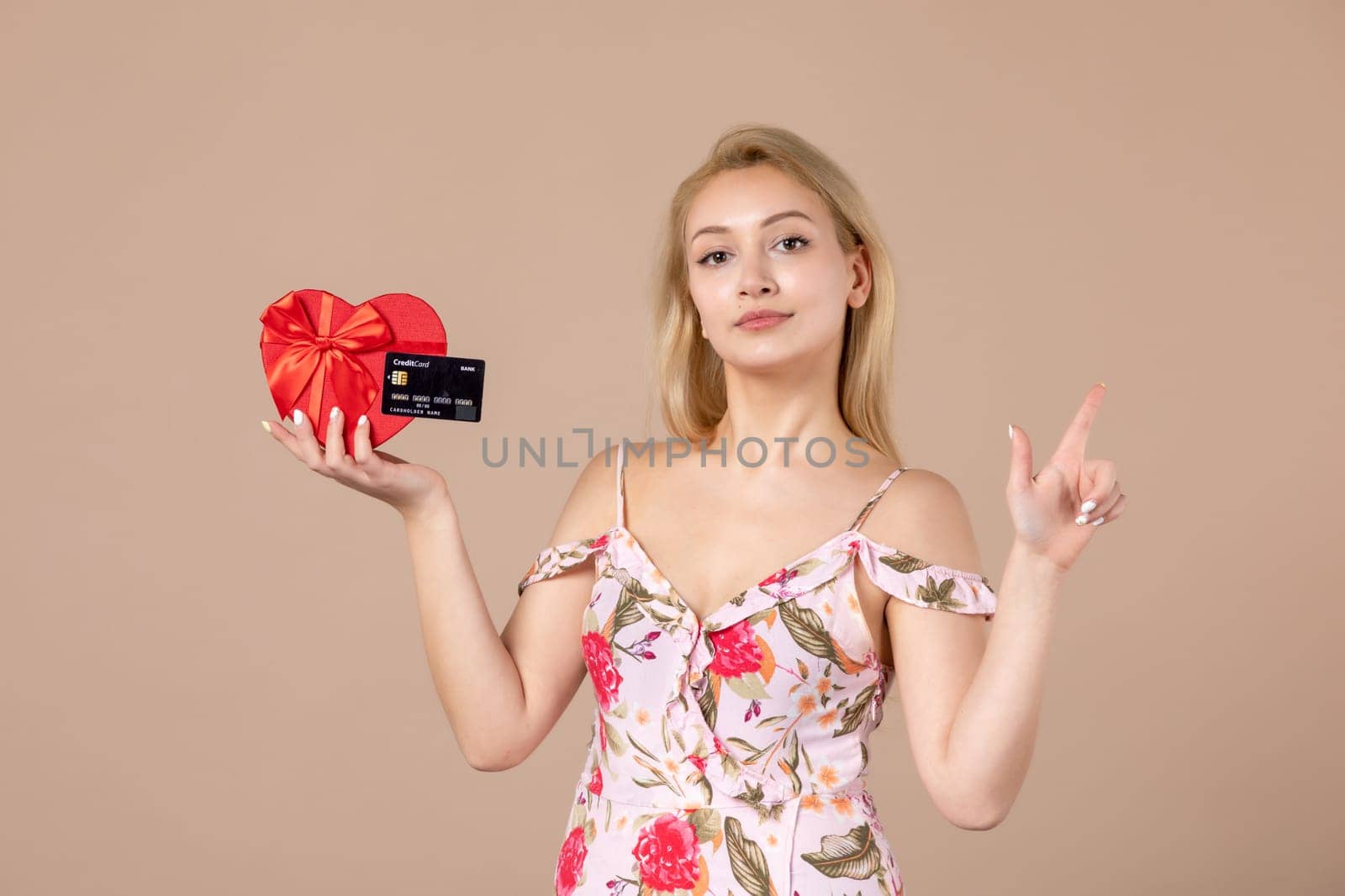 front view young female posing with red heart shaped present and bank card on brown background feminine money march sensual equality woman