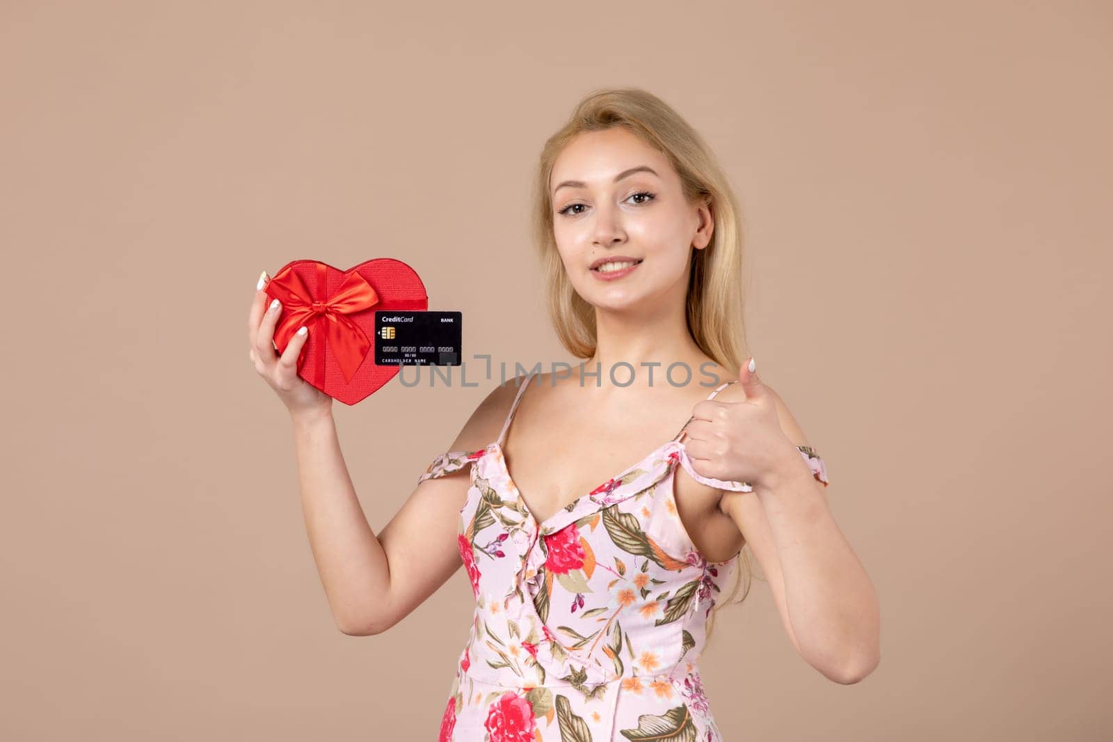 front view young female posing with red heart shaped present and bank card on brown background feminine money march sensual horizontal equality by Kamran