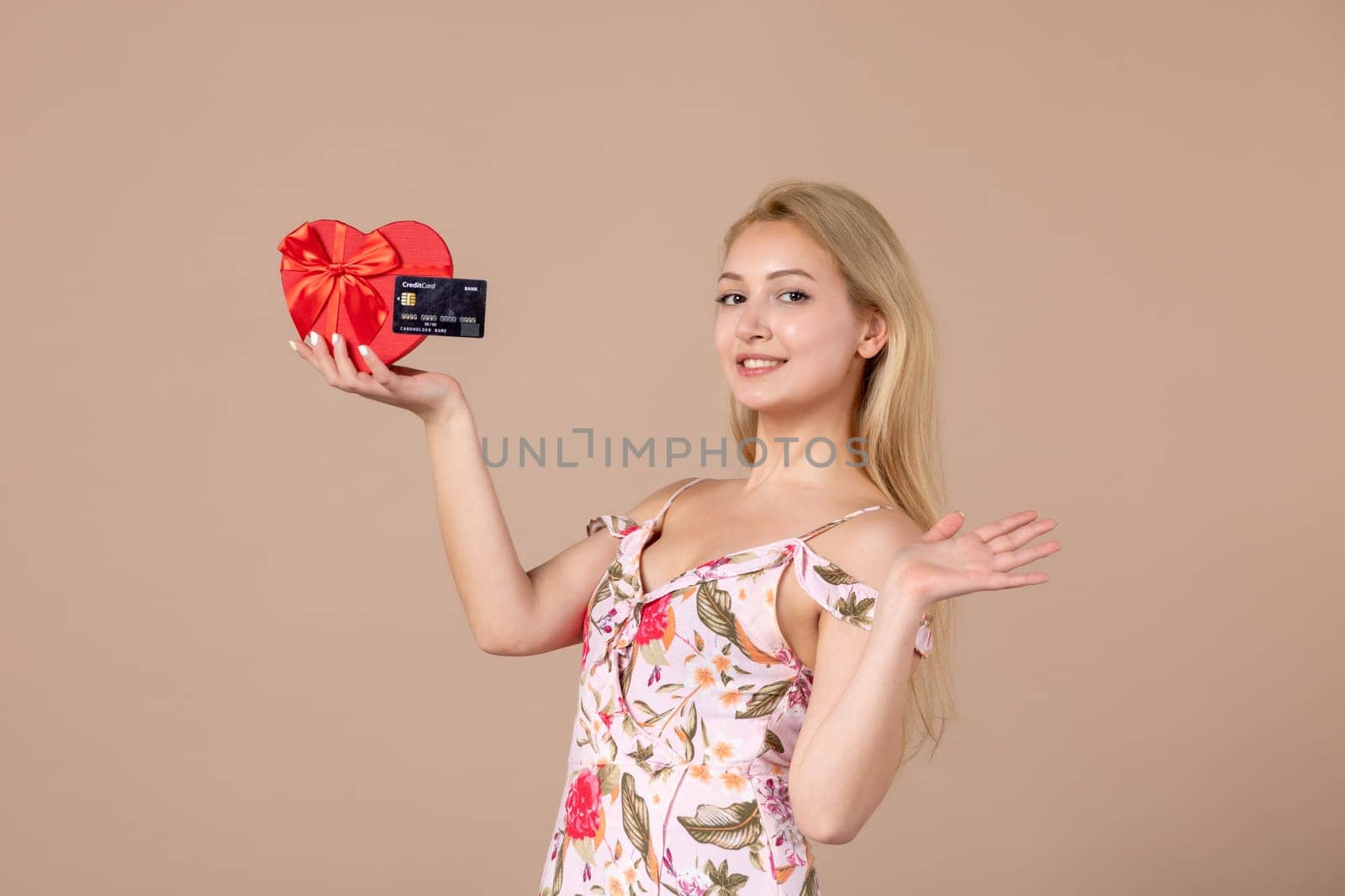 front view young female posing with red heart shaped present and bank card on brown background feminine money march sensual horizontal equality woman by Kamran