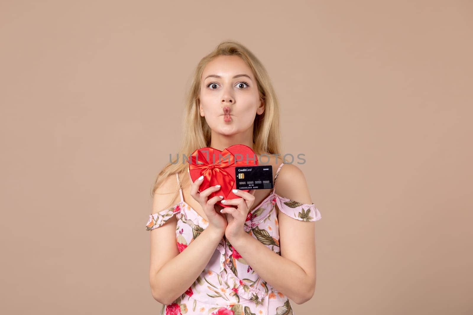 front view young female posing with red heart shaped present and bank card on brown background feminine money march woman sensual equality by Kamran