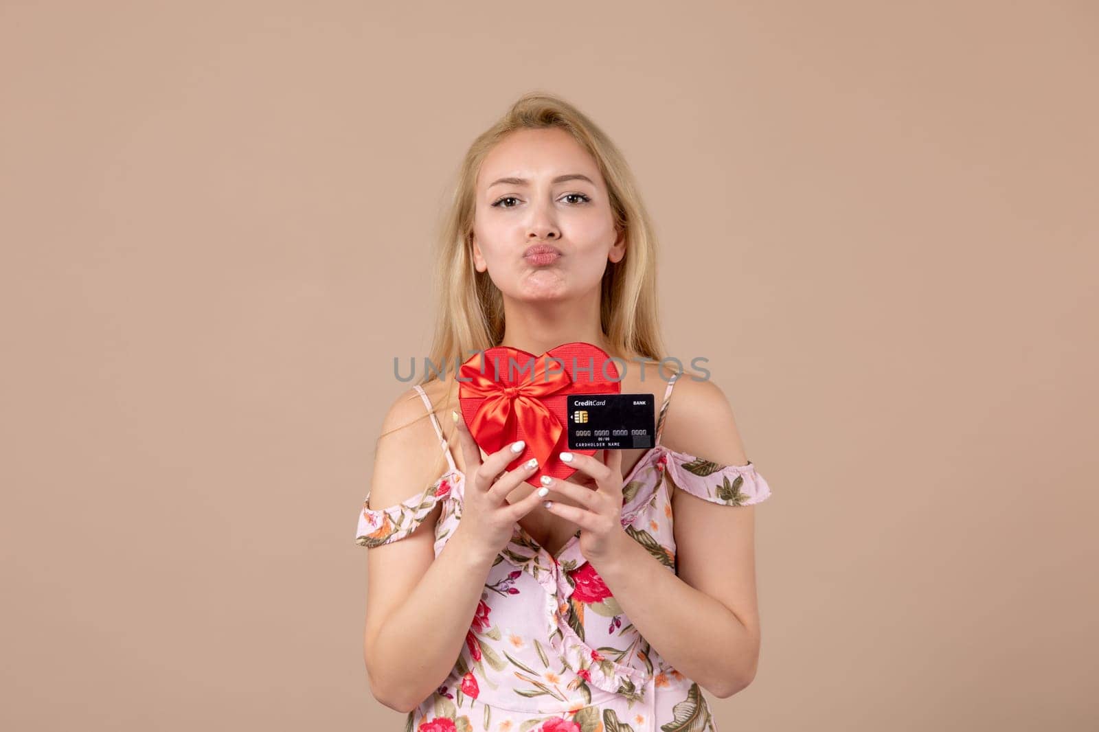 front view young female posing with red heart shaped present and bank card on brown background feminine money march woman sensual horizontal by Kamran