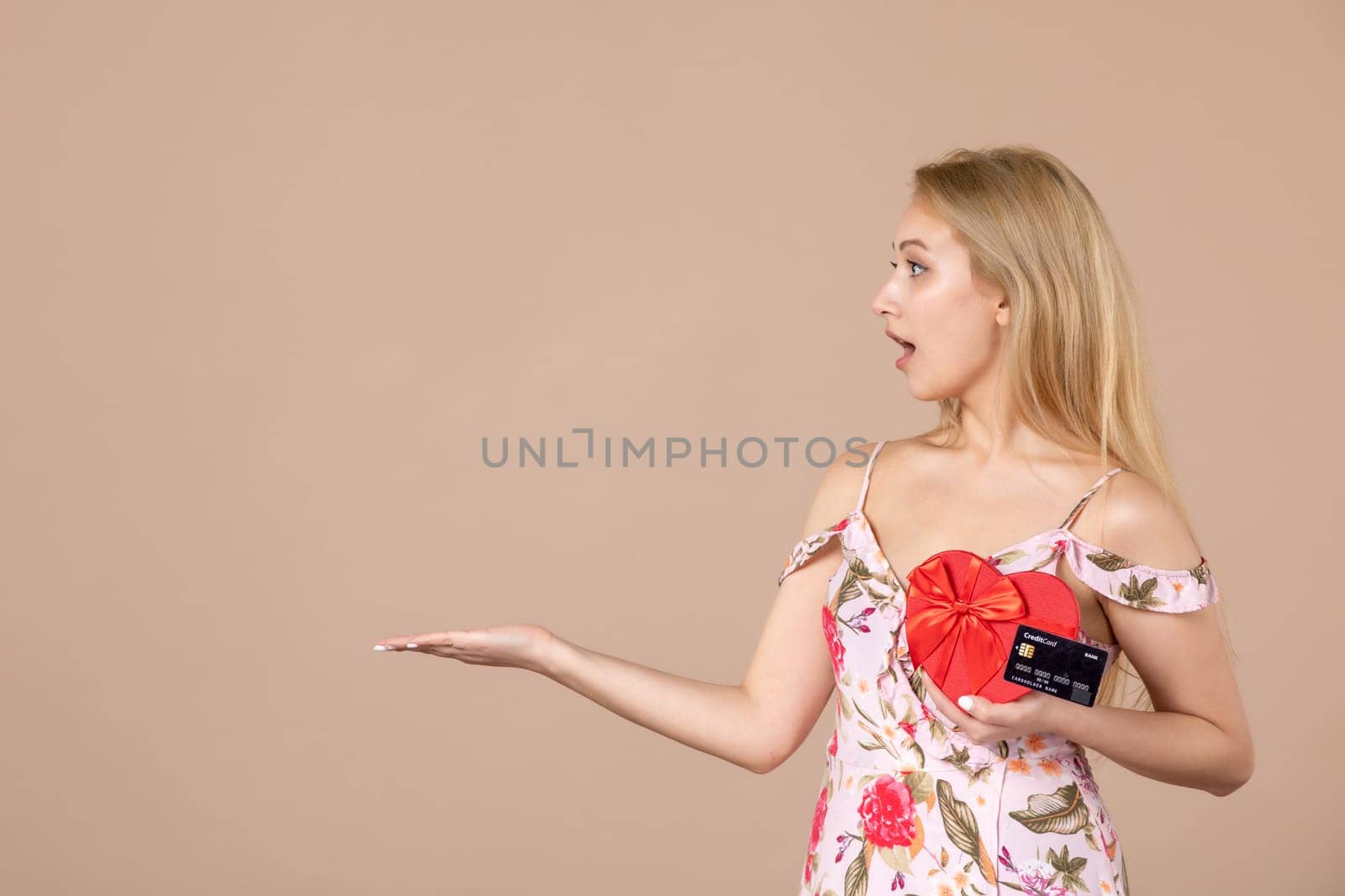 front view young female posing with red heart shaped present and bank card on brown background money march horizontal feminine equality sensual by Kamran