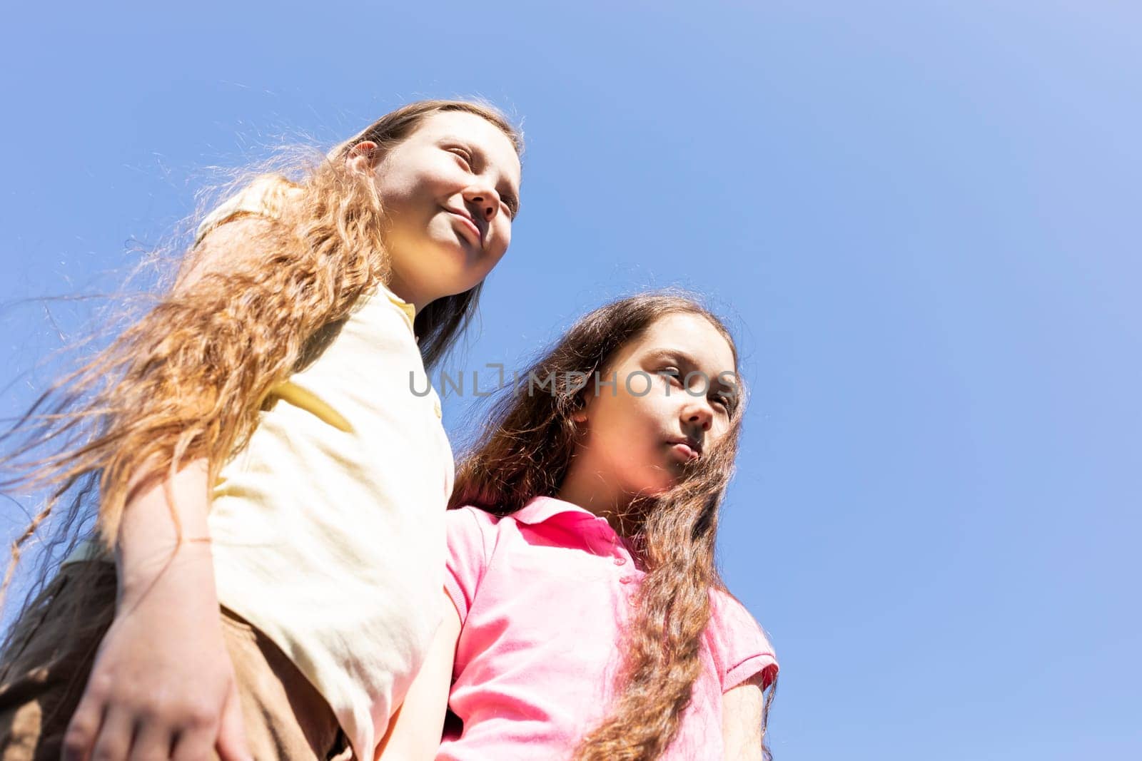 Portrait Smiling Two Pretty Sisters With Extra Long Hair, Blue Sky On Background, Sunny Day, Copy Space. Pretty Siblings Wear Casual Clothes, True Friendship. Horizontal Plane. High quality photo