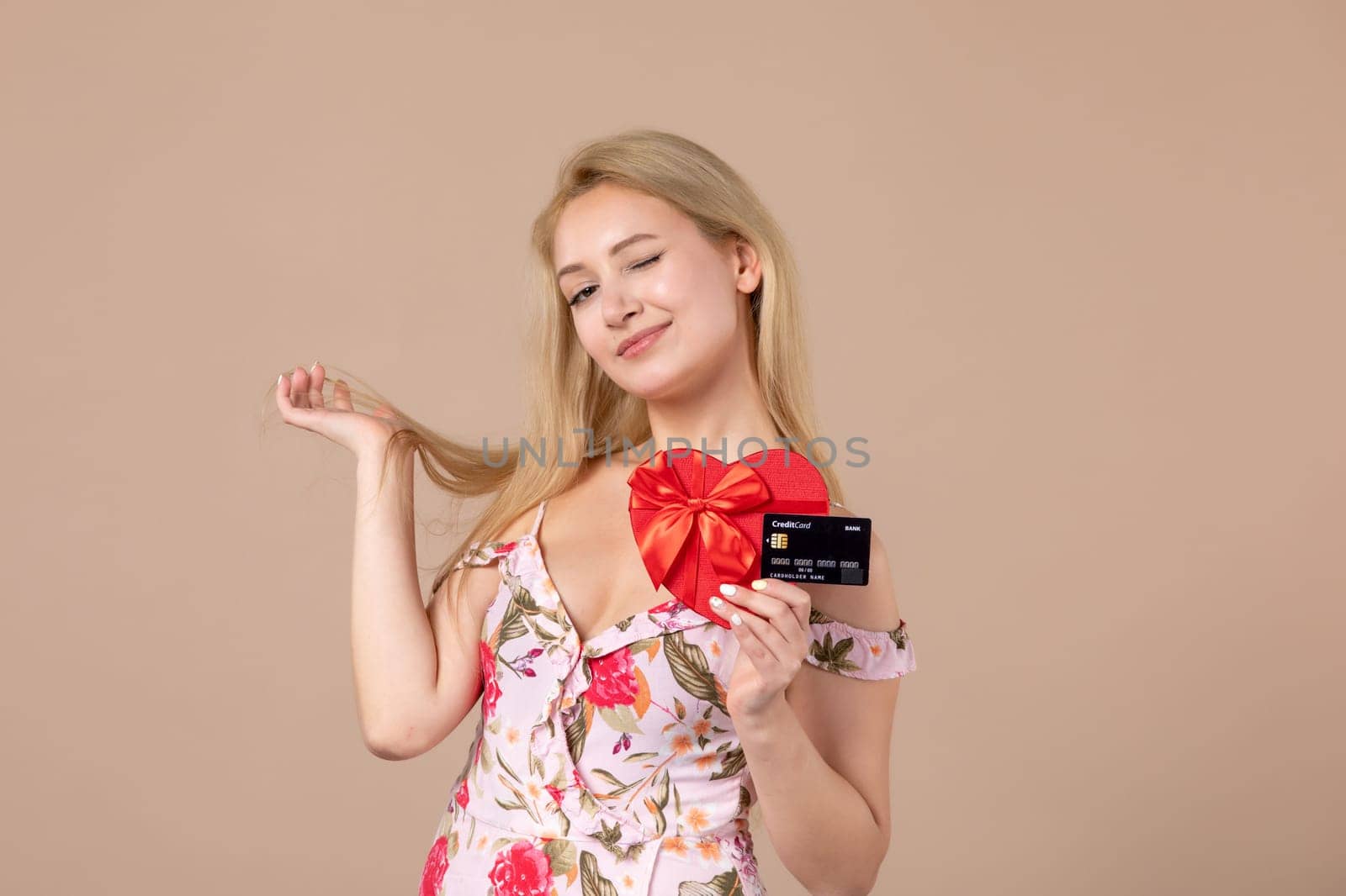 front view young female posing with red heart shaped present and bank card on brown background money march woman sensual horizontal equality by Kamran