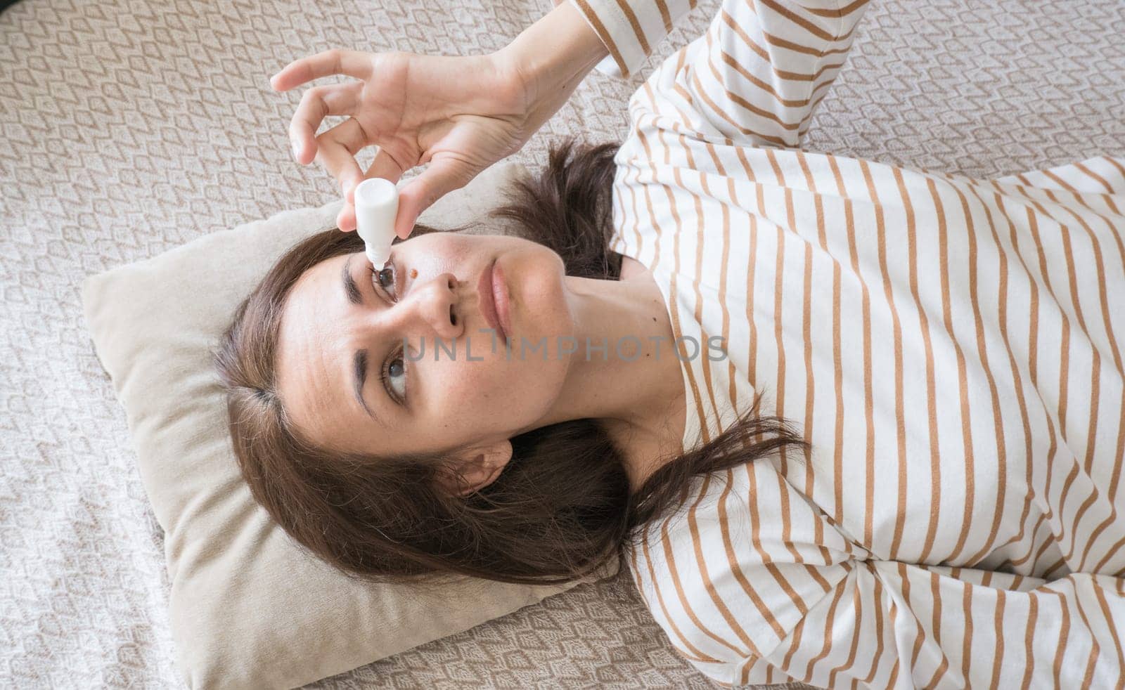 Top view of a woman who drips antibacterial drops into her eyes while lying on the couch.