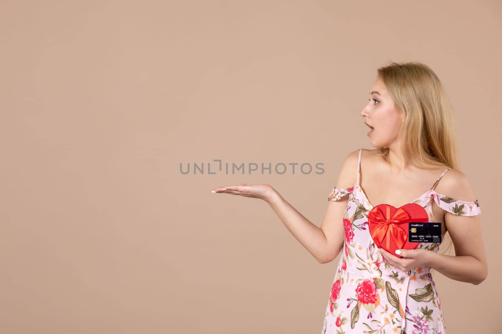 front view young female posing with red heart shaped present and bank card on brown background money equality feminine march horizontal woman by Kamran