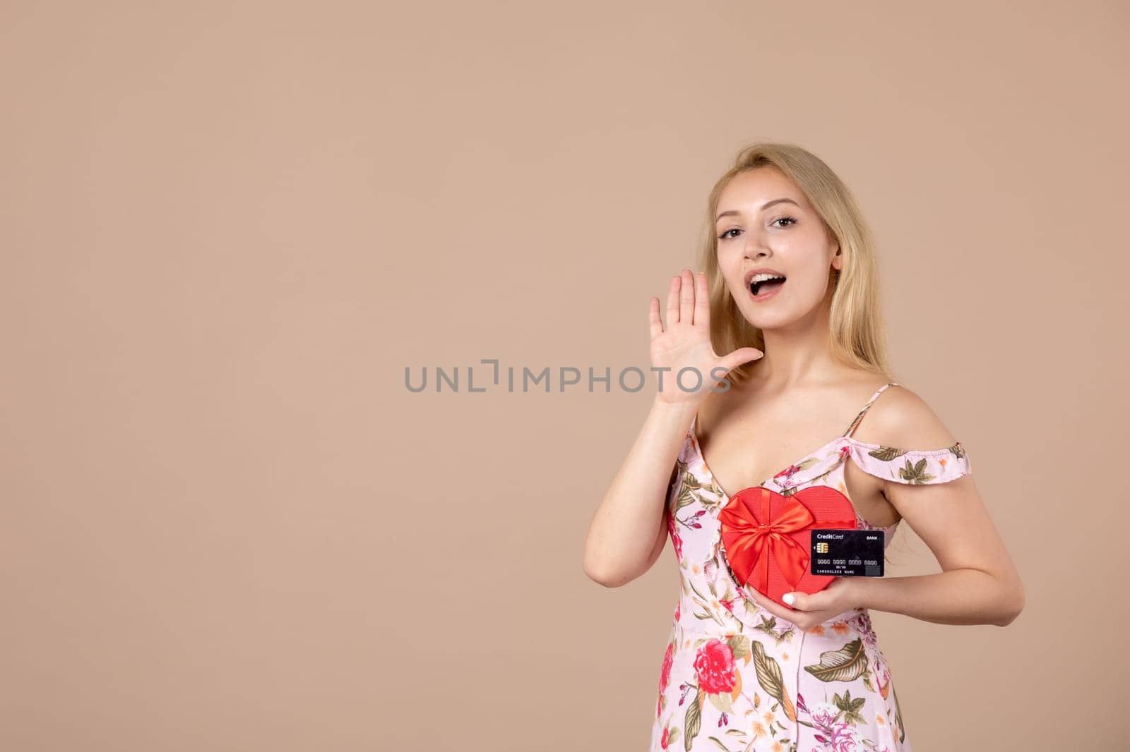 front view young female posing with red heart shaped present and bank card on brown background money equality sensual march horizontal woman feminine by Kamran