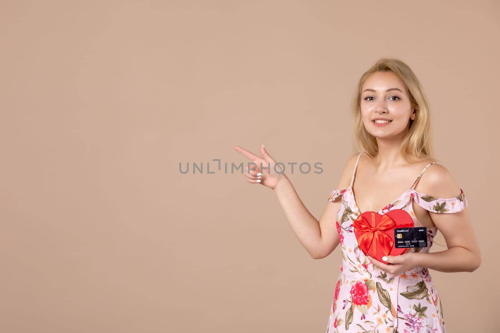 front view young female posing with red heart shaped present and bank card on brown background money equality sensual feminine march horizontal woman by Kamran