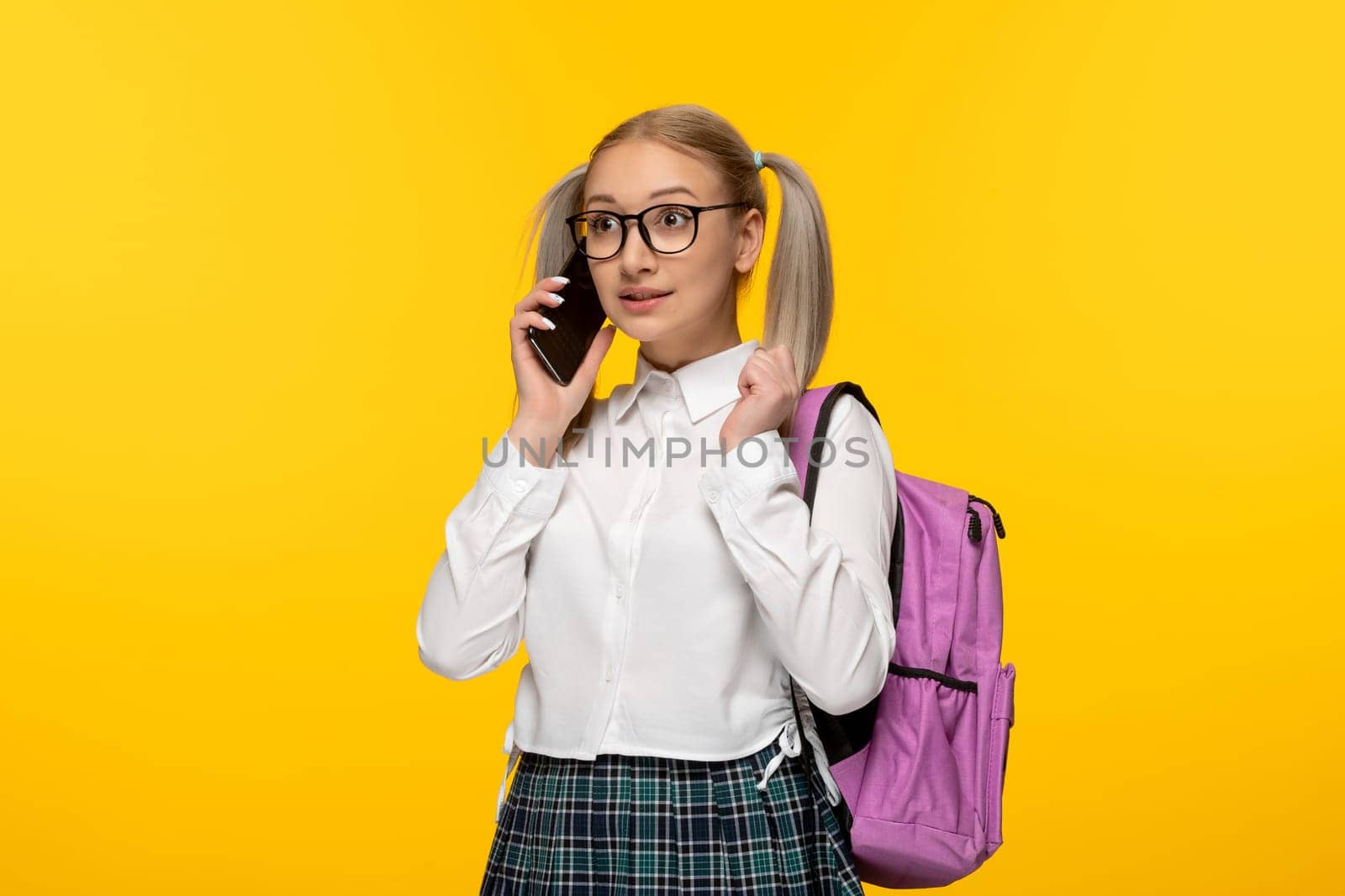 world book day blonde schoolgirl talking on the cellphone on yellow background