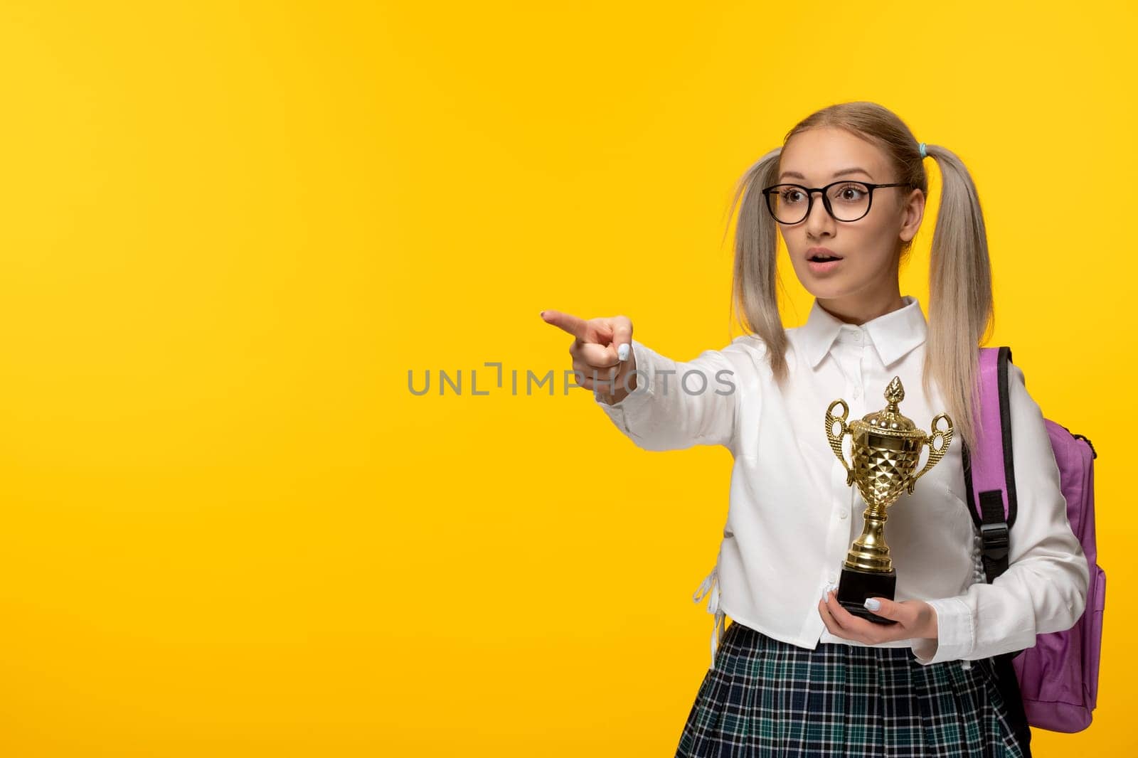 world book day blonde cute schoolgirl in uniform pointing left and holding a trophy