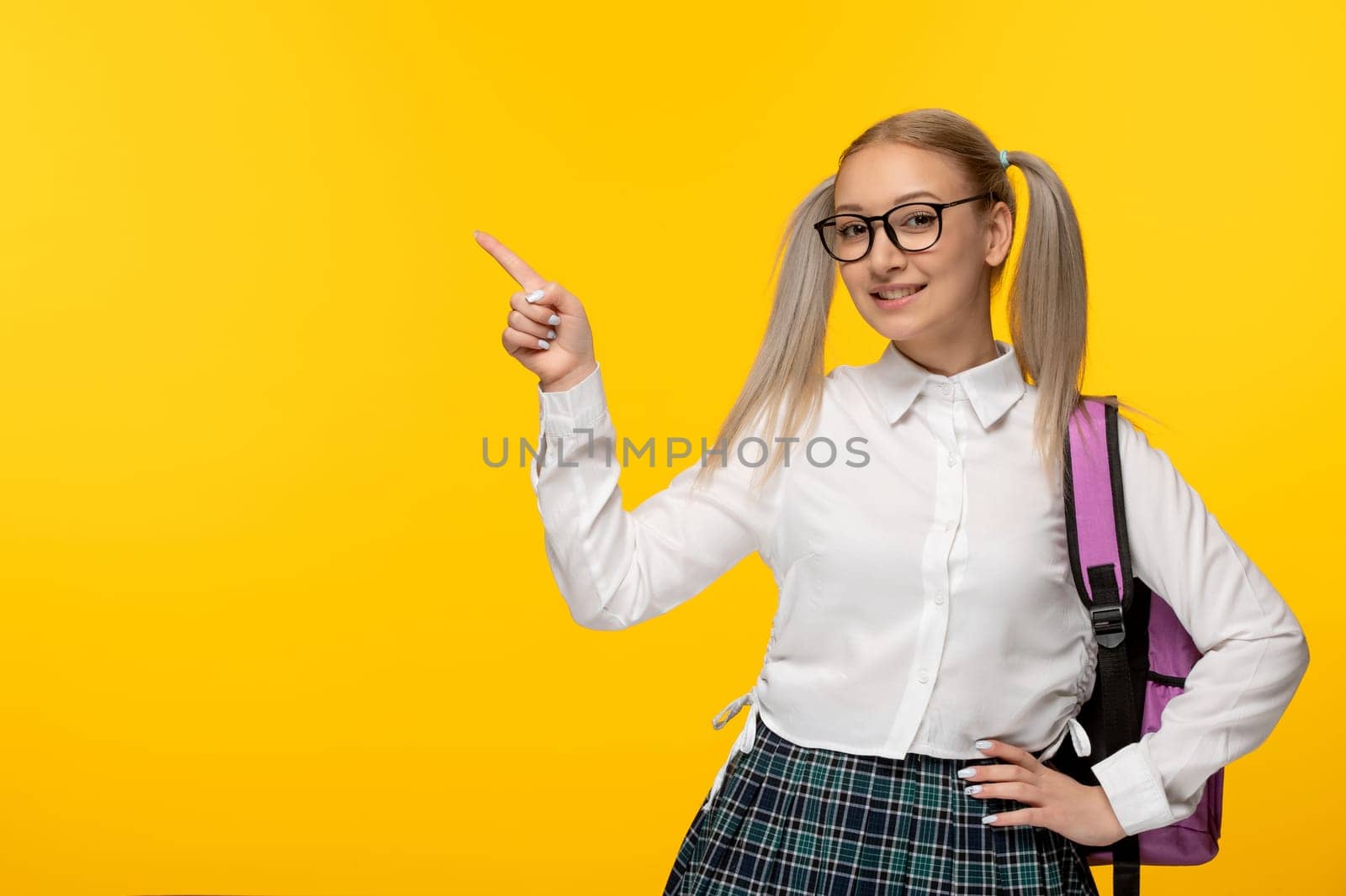 world book day blonde girl with ponytails on yellow background pointing finger in glasses pink backpack by Kamran